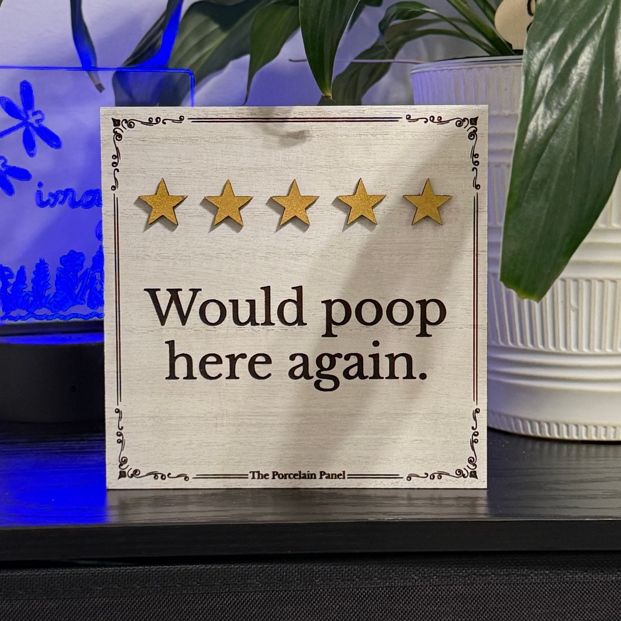Wooden shelf sitter sign reading would poop here again with five gold stars displayed on a tabletop shelf