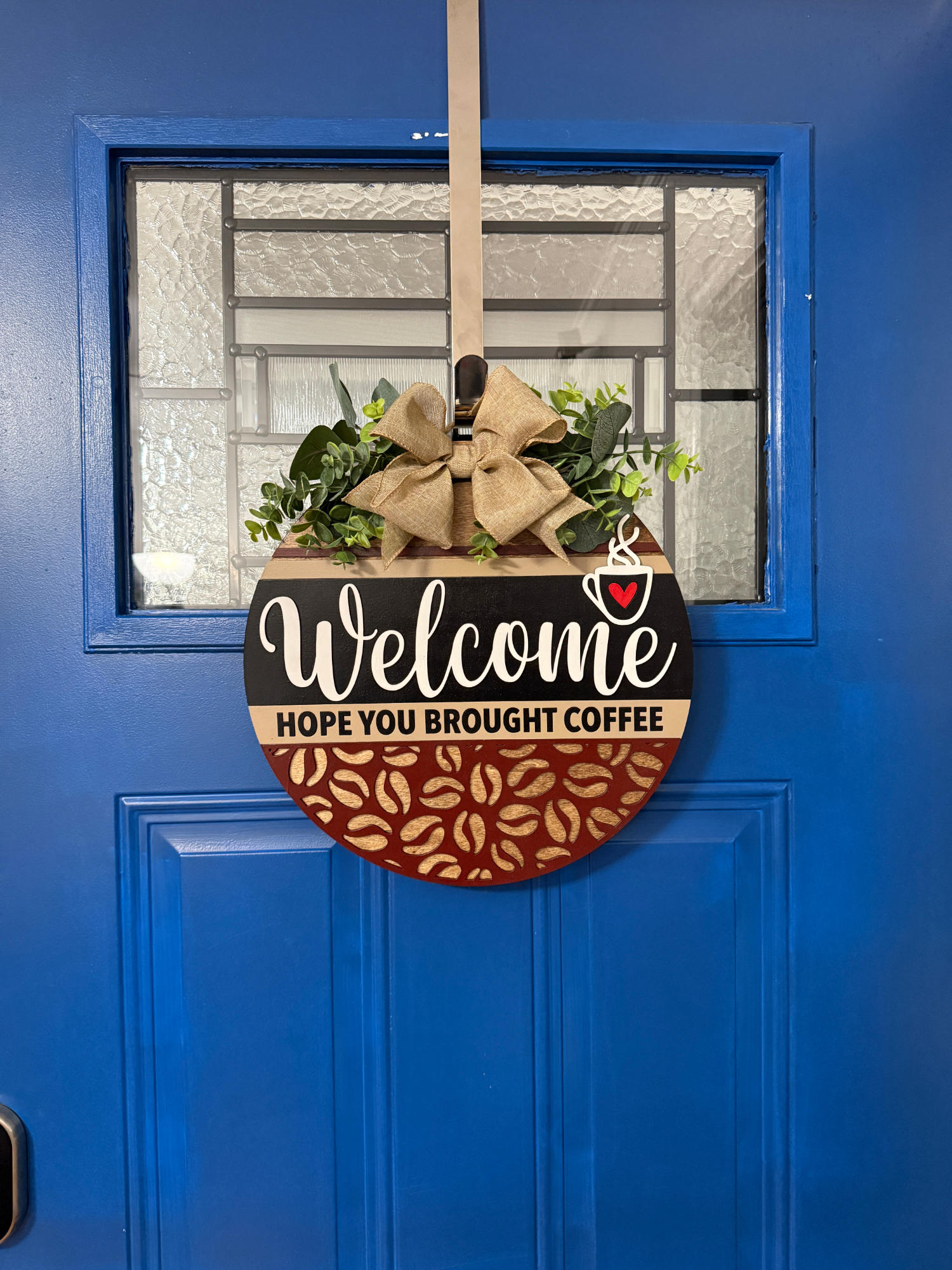 Full view of round coffee welcome sign displayed on front door with neutral decor