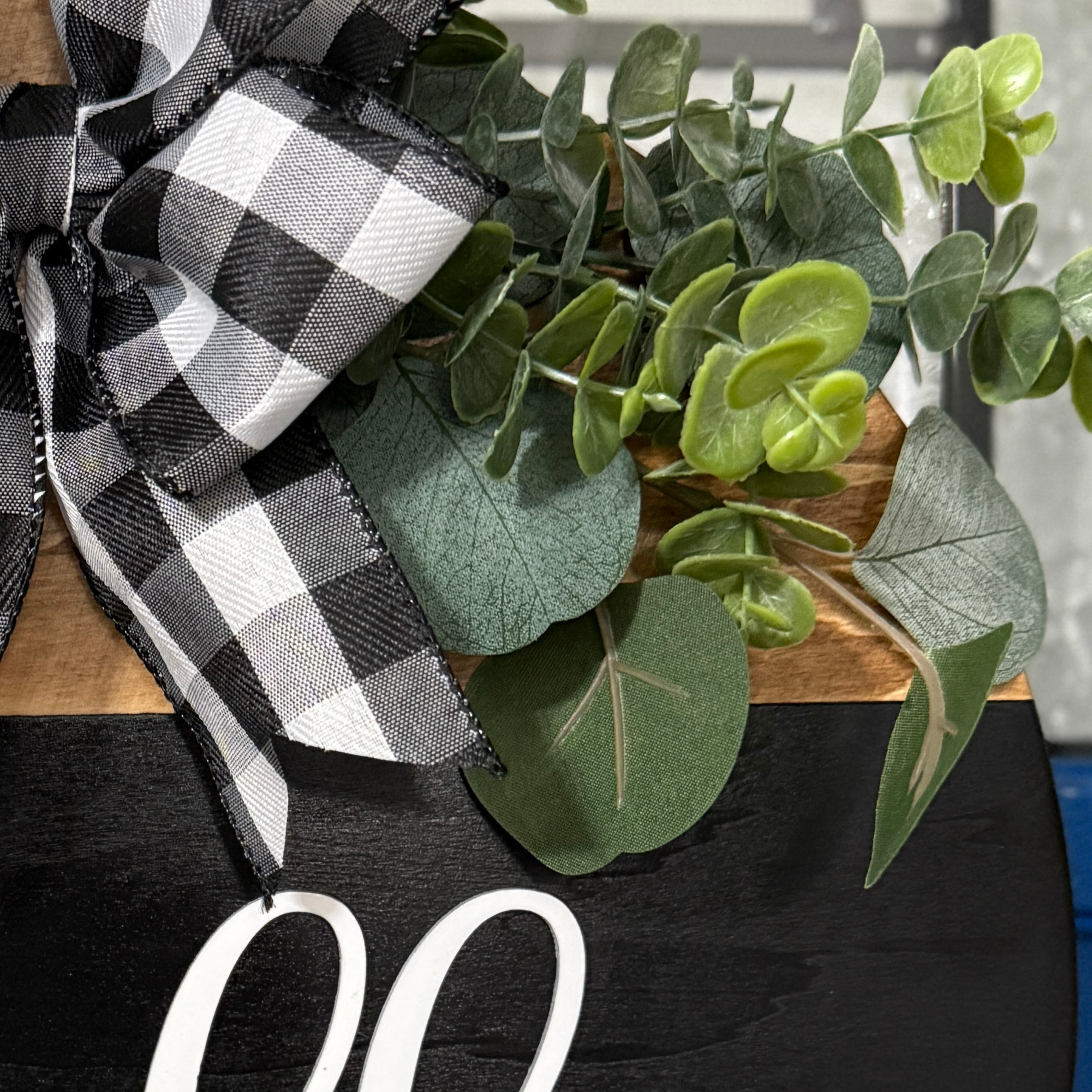 Detailed view of buffalo plaid ribbon and faux greenery on rustic round hello door sign