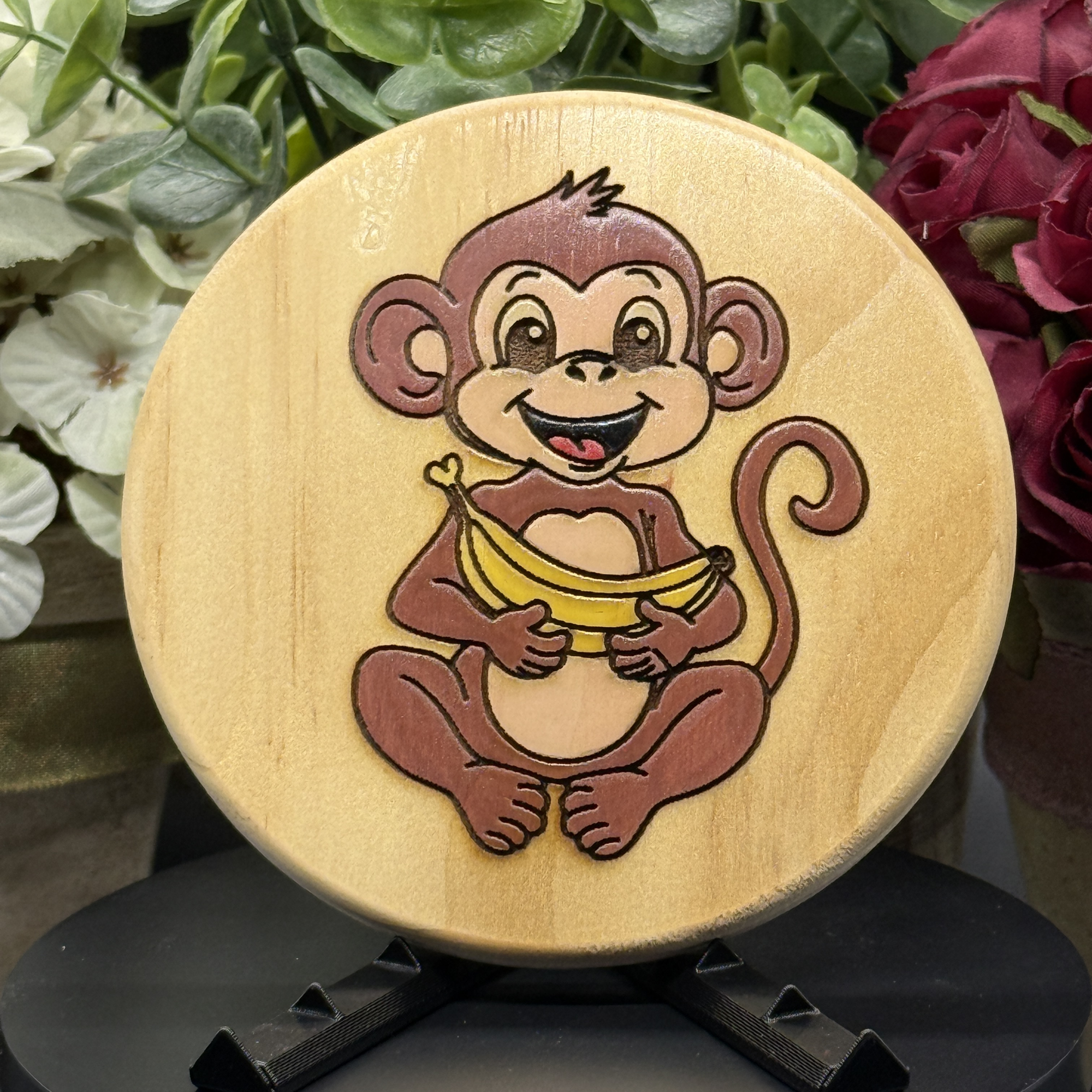 Round pine wood coaster with hand-painted smiling monkey holding a banana, engraved and colored with playful detail