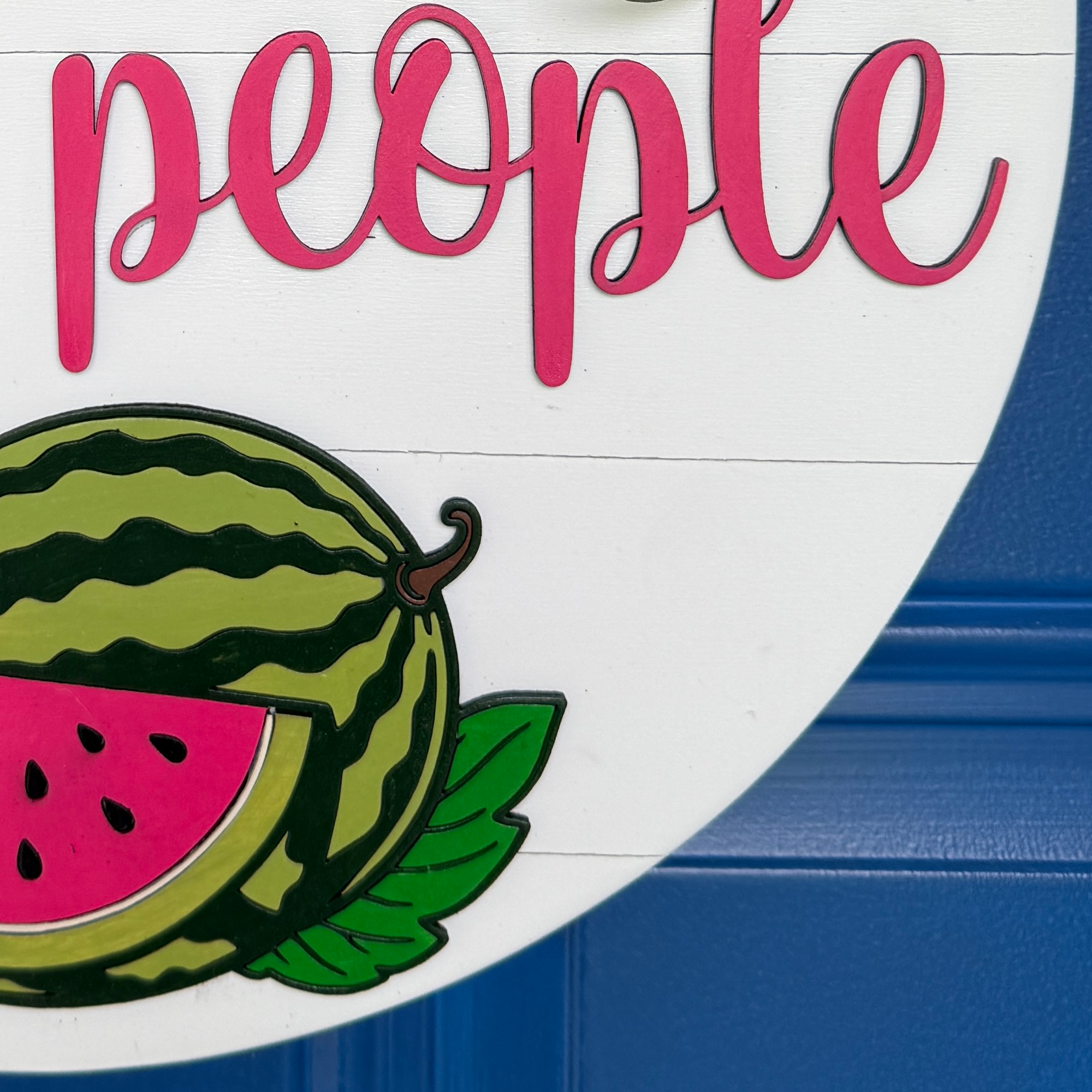 Detailed view of watermelon artwork and Lovely People script lettering on a summer-inspired wood door hanger.