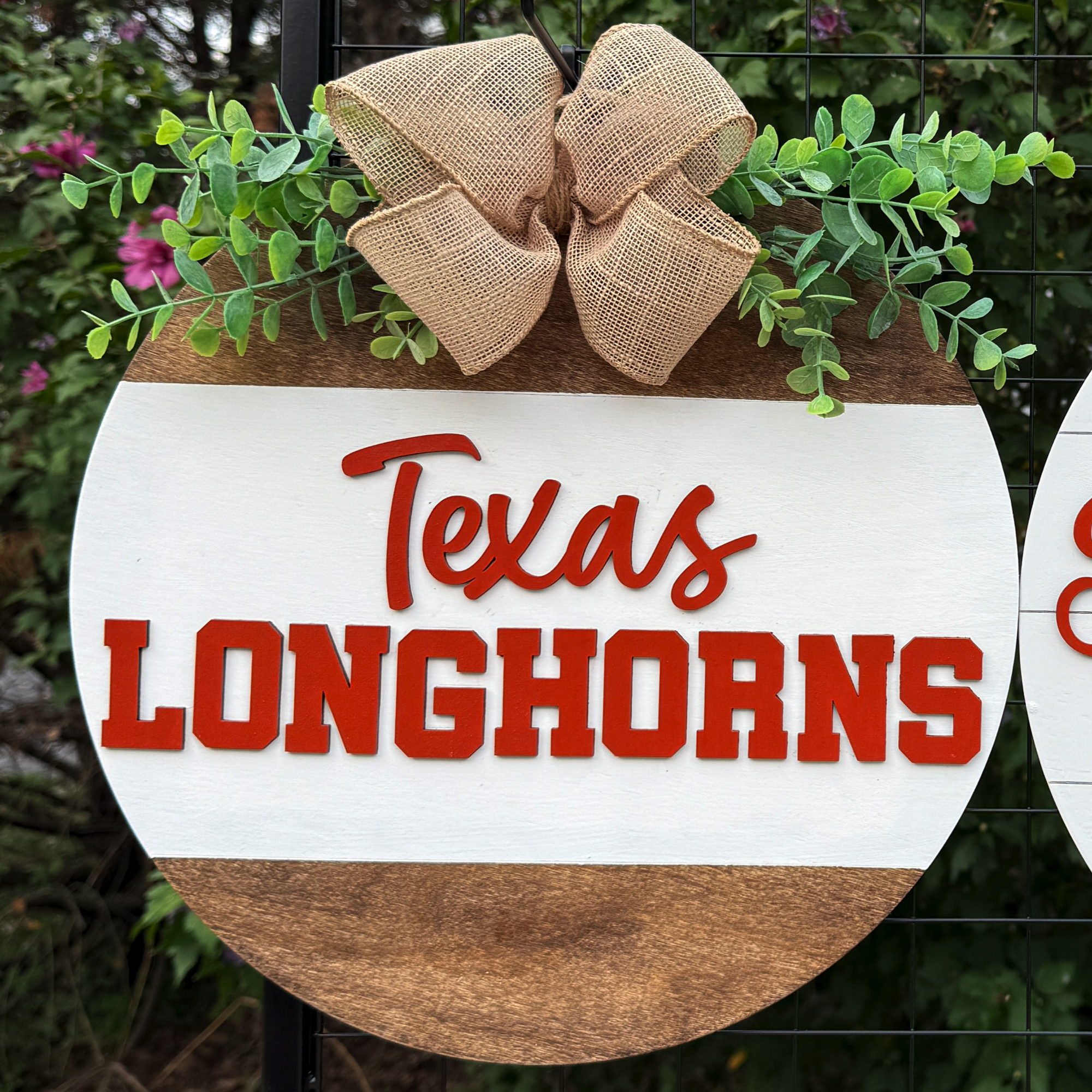 Round Texas Longhorns door hanger with burnt orange lettering, greenery accents, and burlap bow on rustic wood background