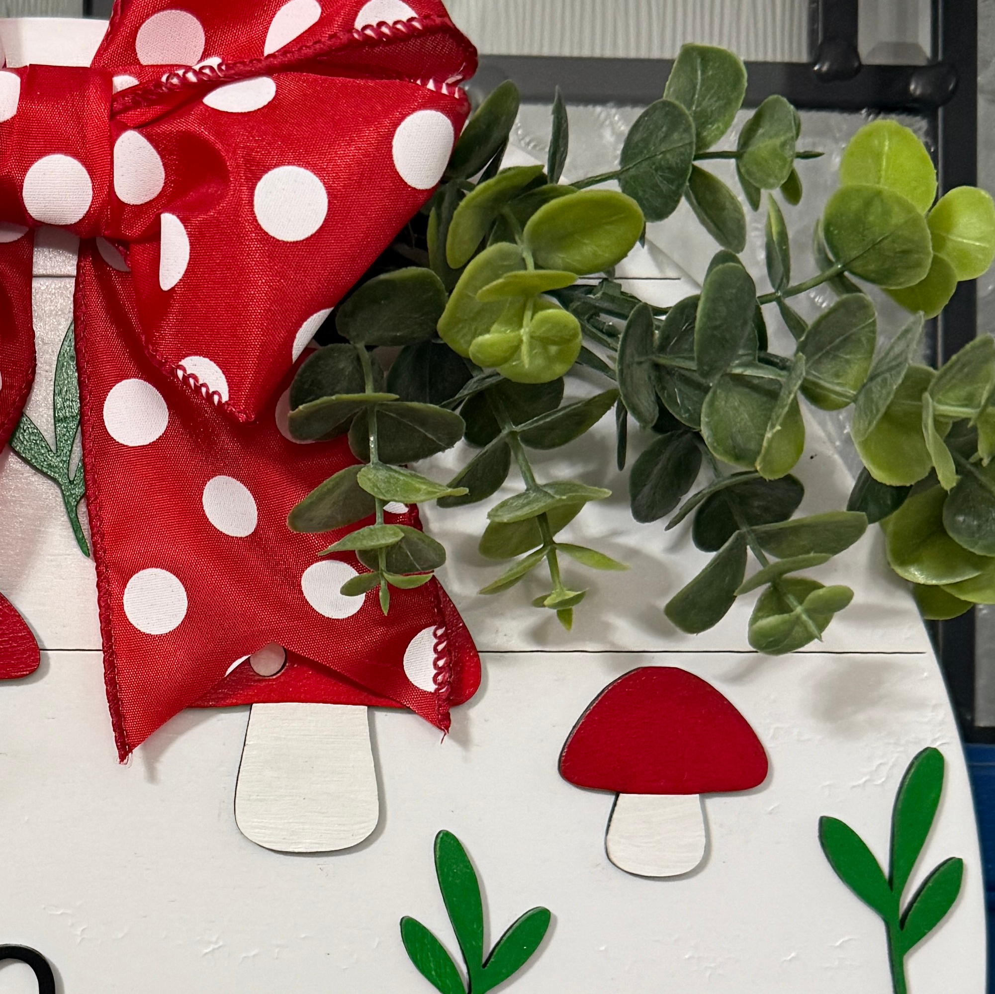 Close-up of red polka dot bow and eucalyptus greenery on wood sign