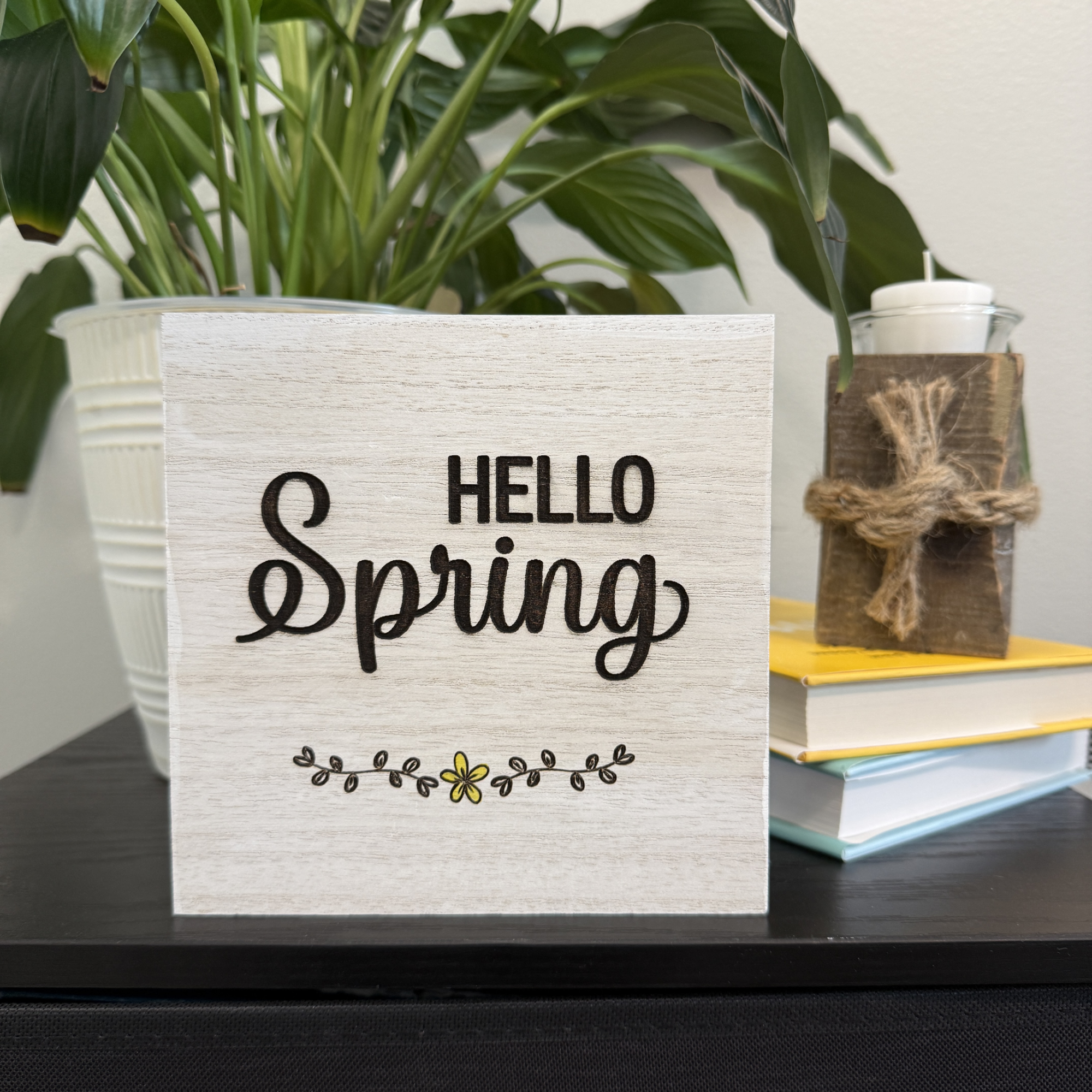 Hello Spring wooden shelf sitter styled on a shelf with stacked books, white planter, and trailing green plant