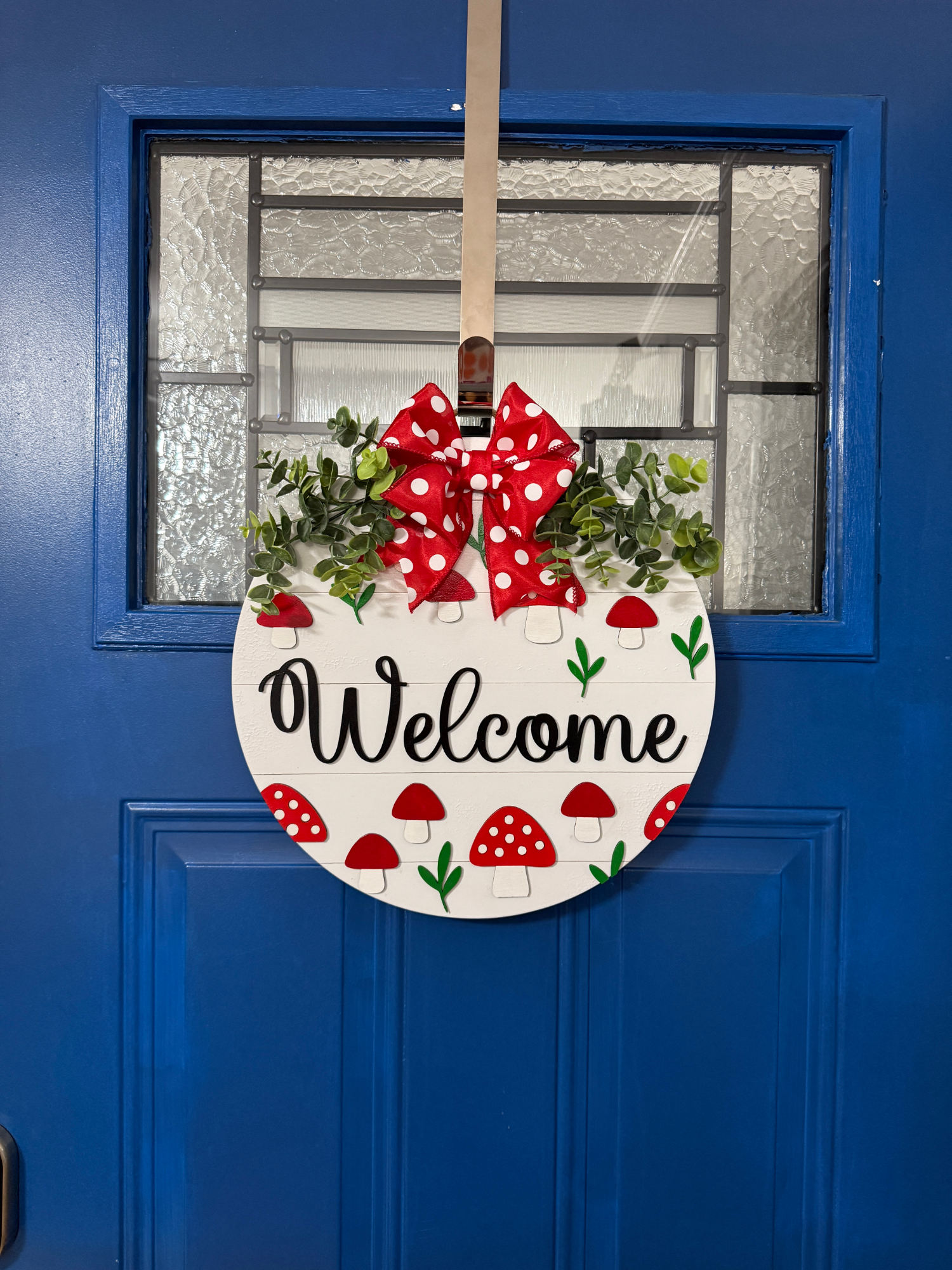 Round wood door hanger featuring red mushrooms and white shiplap background on blue door