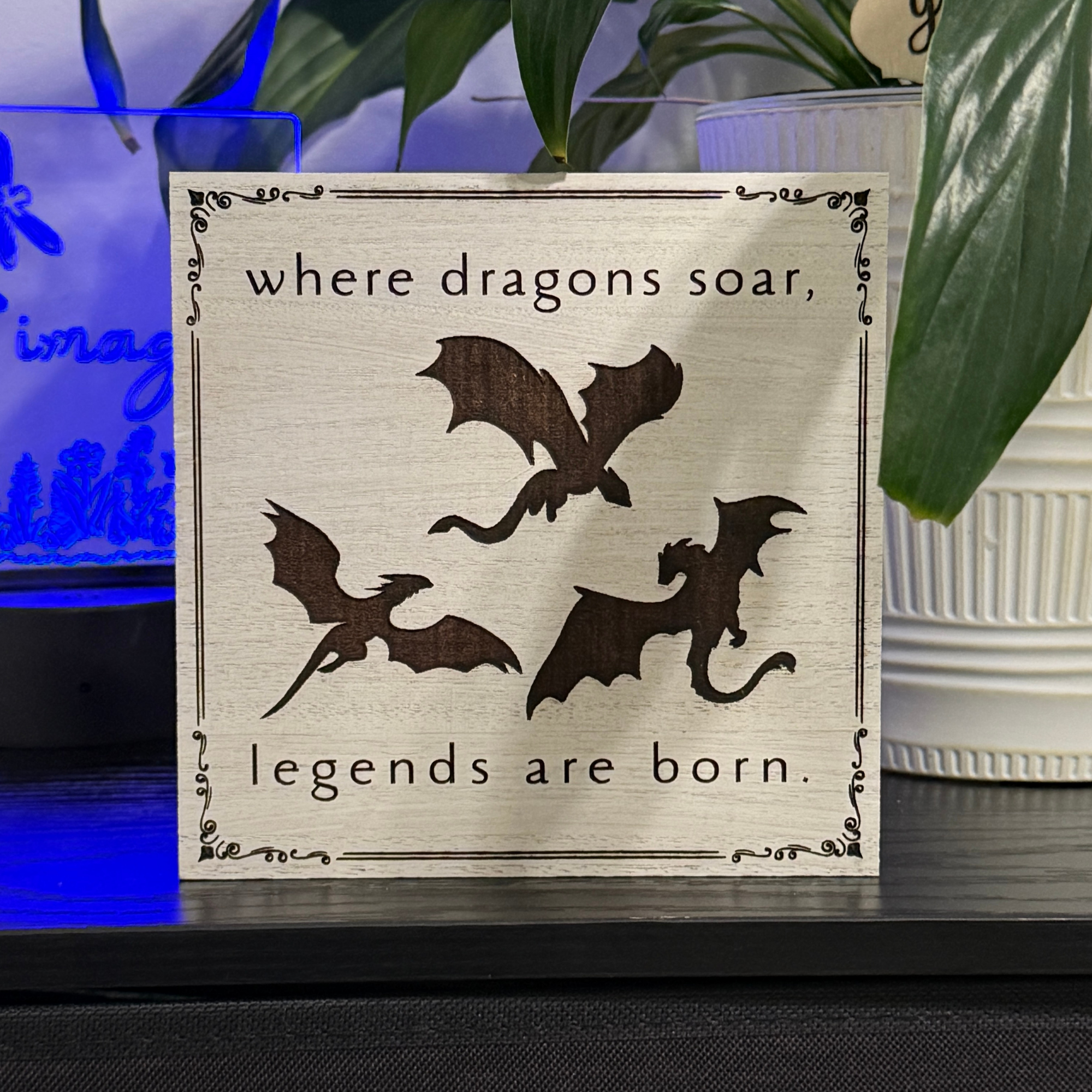 Wooden sign reading where dragons soar legends are born with flying dragon silhouettes displayed with blue accent lighting