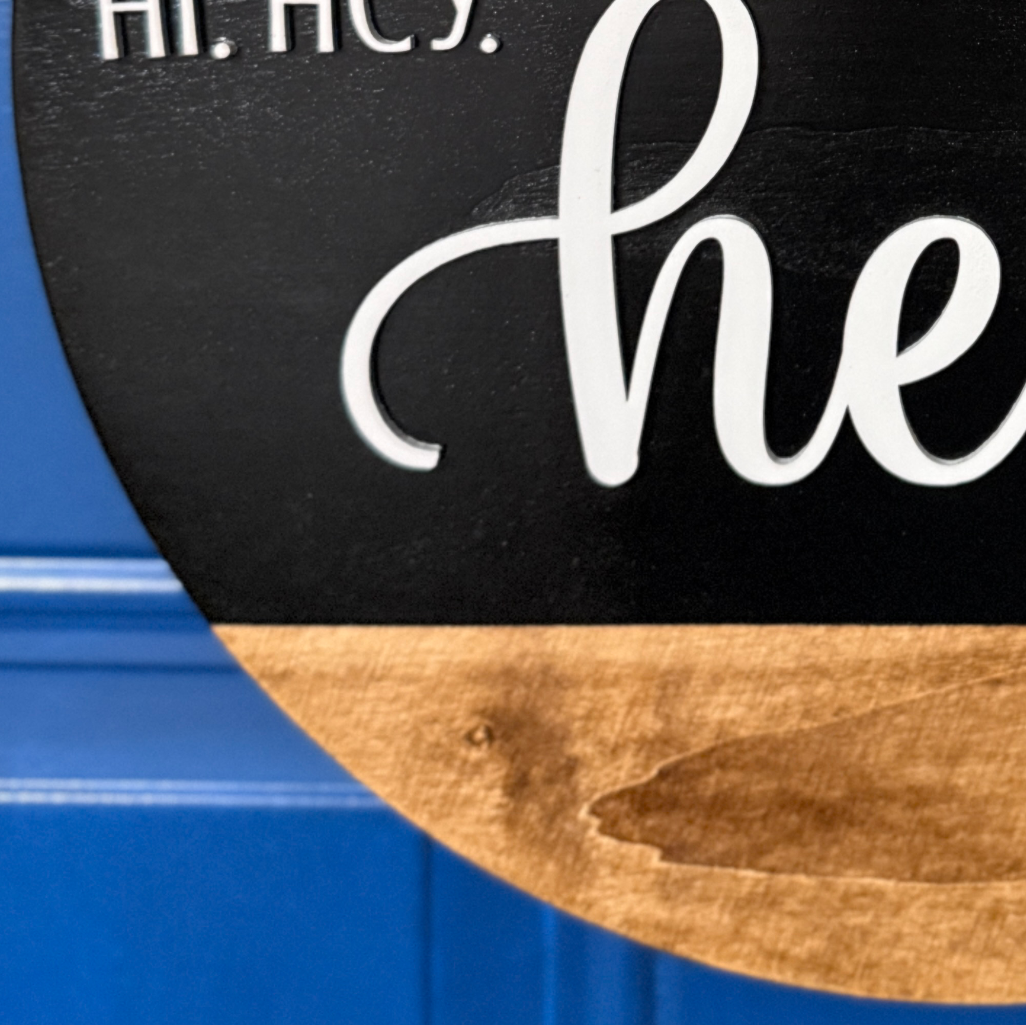 Close-up of white hello script lettering on black painted wood door hanger with natural stained wood accent