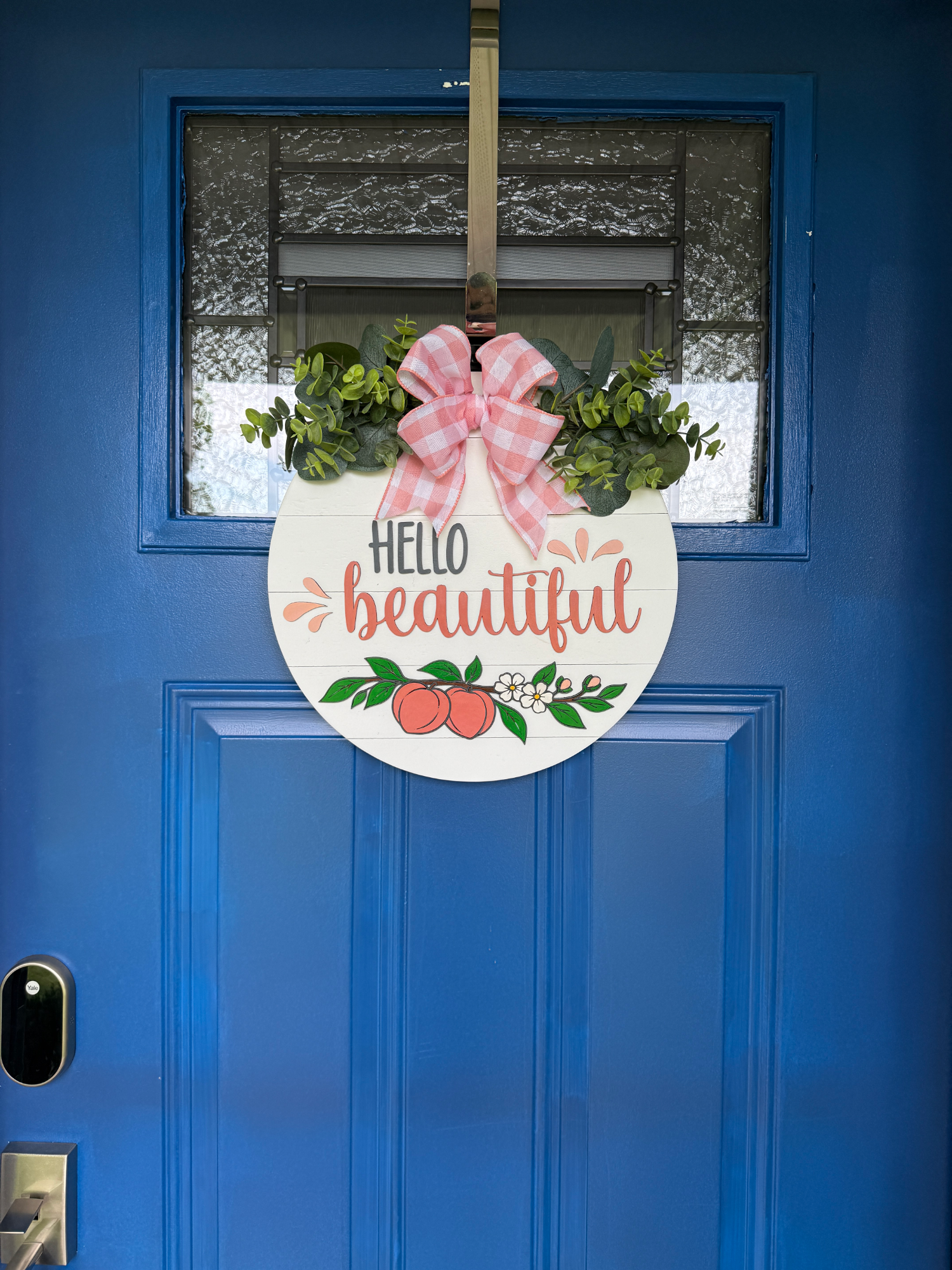 Peach-themed front door hanger displayed on a blue entry door with pink gingham bow, greenery, and Hello Beautiful greeting.
