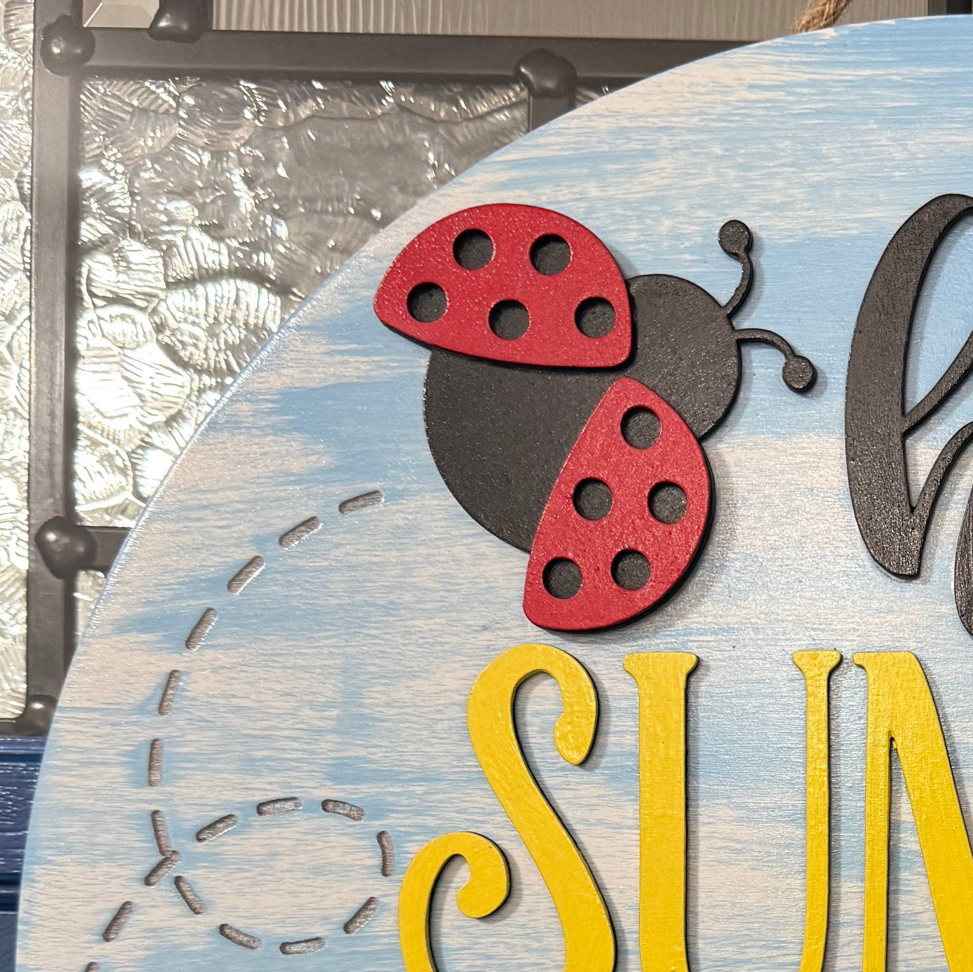 Close-up of ladybug detail on hello summer sign with textured painted wood background