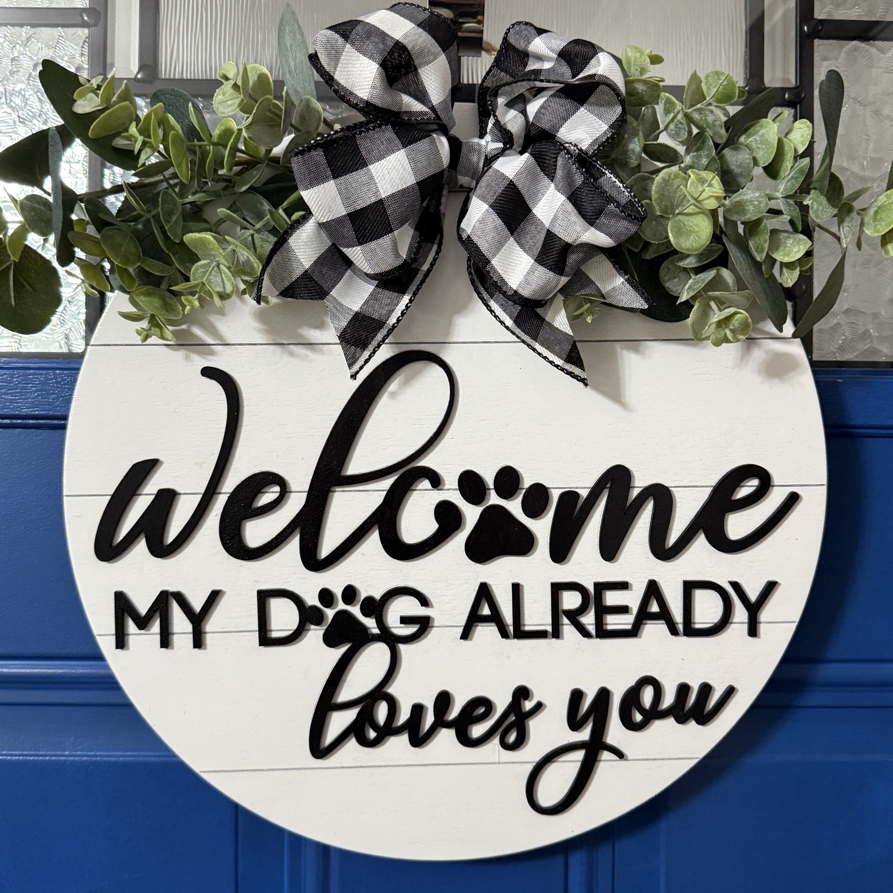 Full view of round white welcome sign with paw print detail and “my dog already loves you” message
