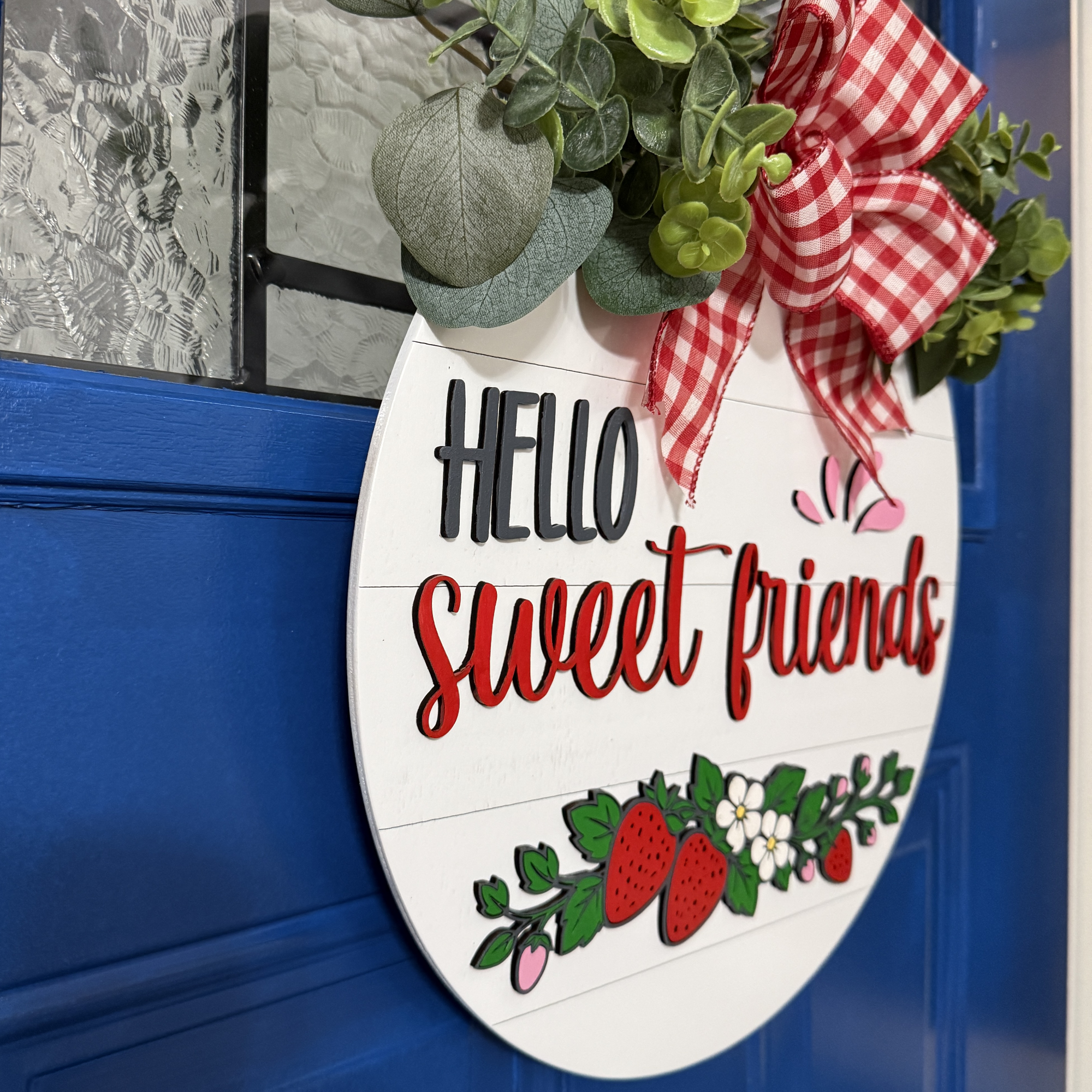 Angled side view of Hello Sweet Friends round wood door hanger showing layered thickness, greenery, and dimensional lettering