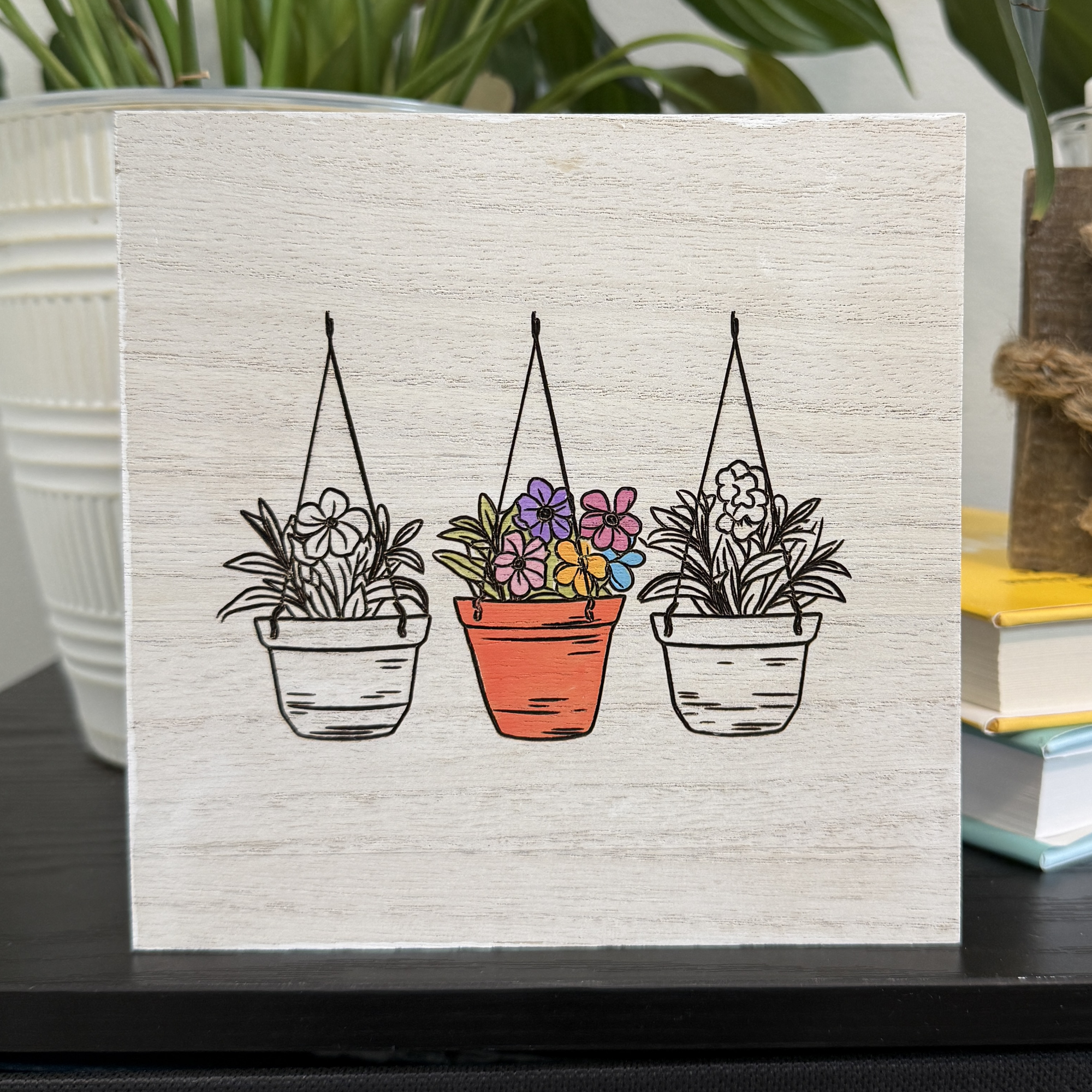 Hanging planter wood shelf sitter featuring three hanging flower pots with hand-painted terracotta center planter displayed on a shelf with plant and books