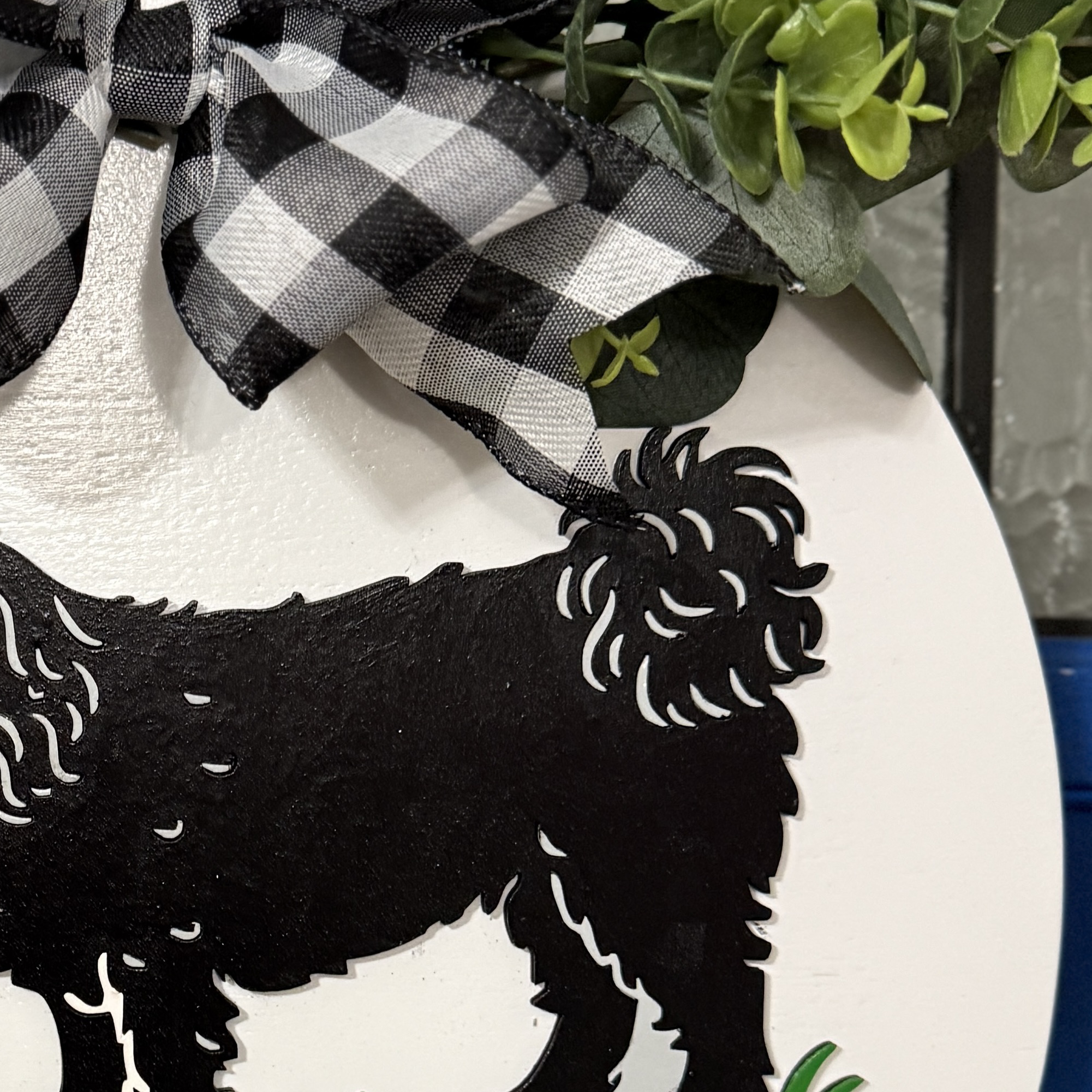 Detailed view of black and white buffalo check bow with layered greenery on top of dog-themed door decor
