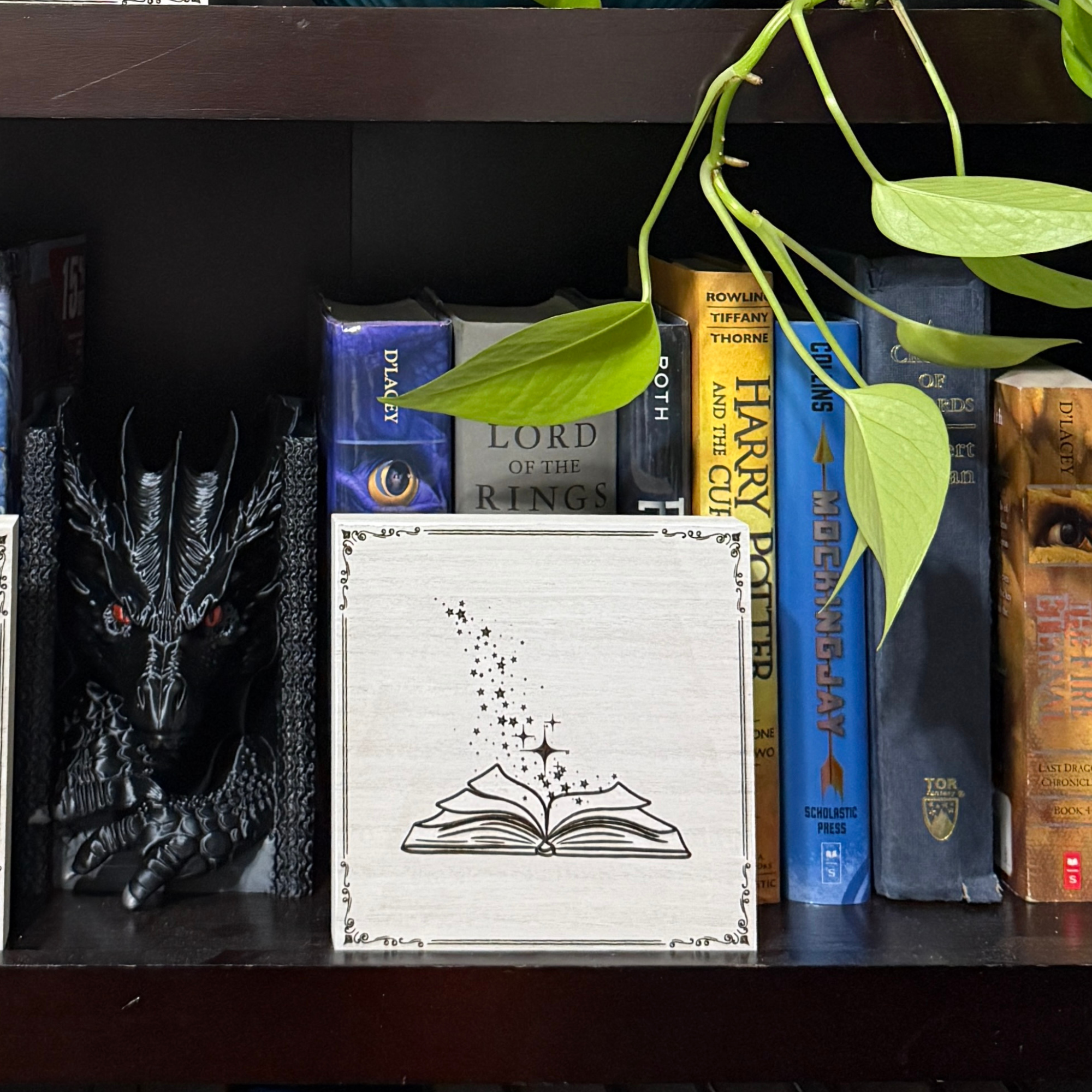 Magic book shelf sitter displayed on a bookshelf with fantasy novels and dragon decor, highlighting engraved star and spark details