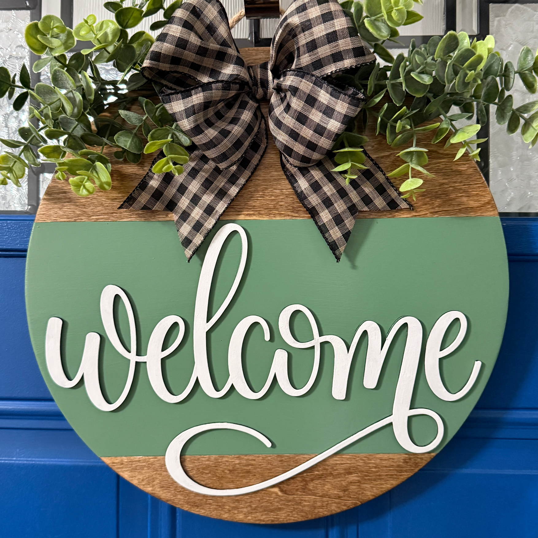 Welcome door hanger on stained base with sage green background, faux with greenery and coordinating bow