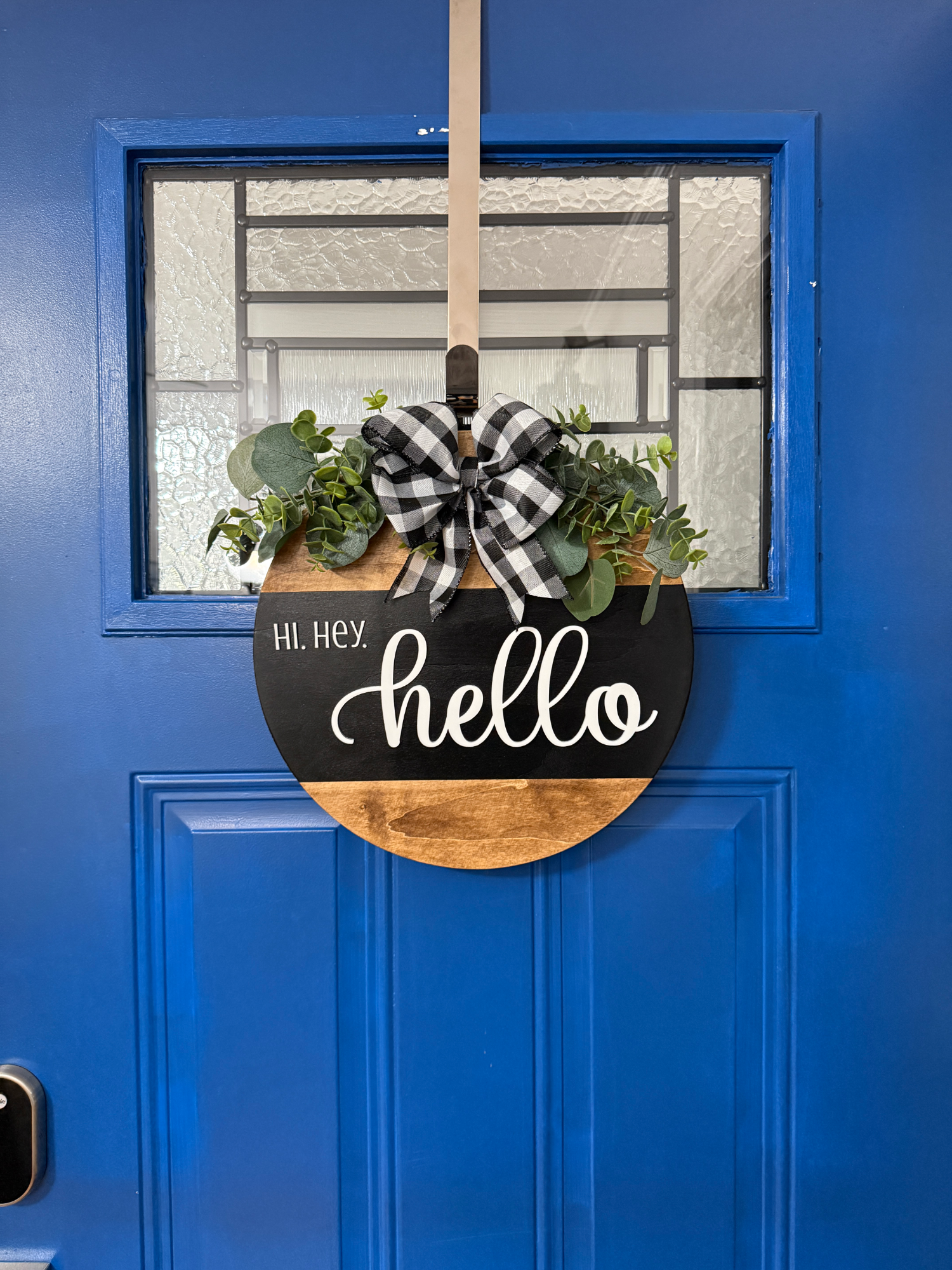 Full front door display featuring black and natural wood hello door hanger with greenery and plaid ribbon bow