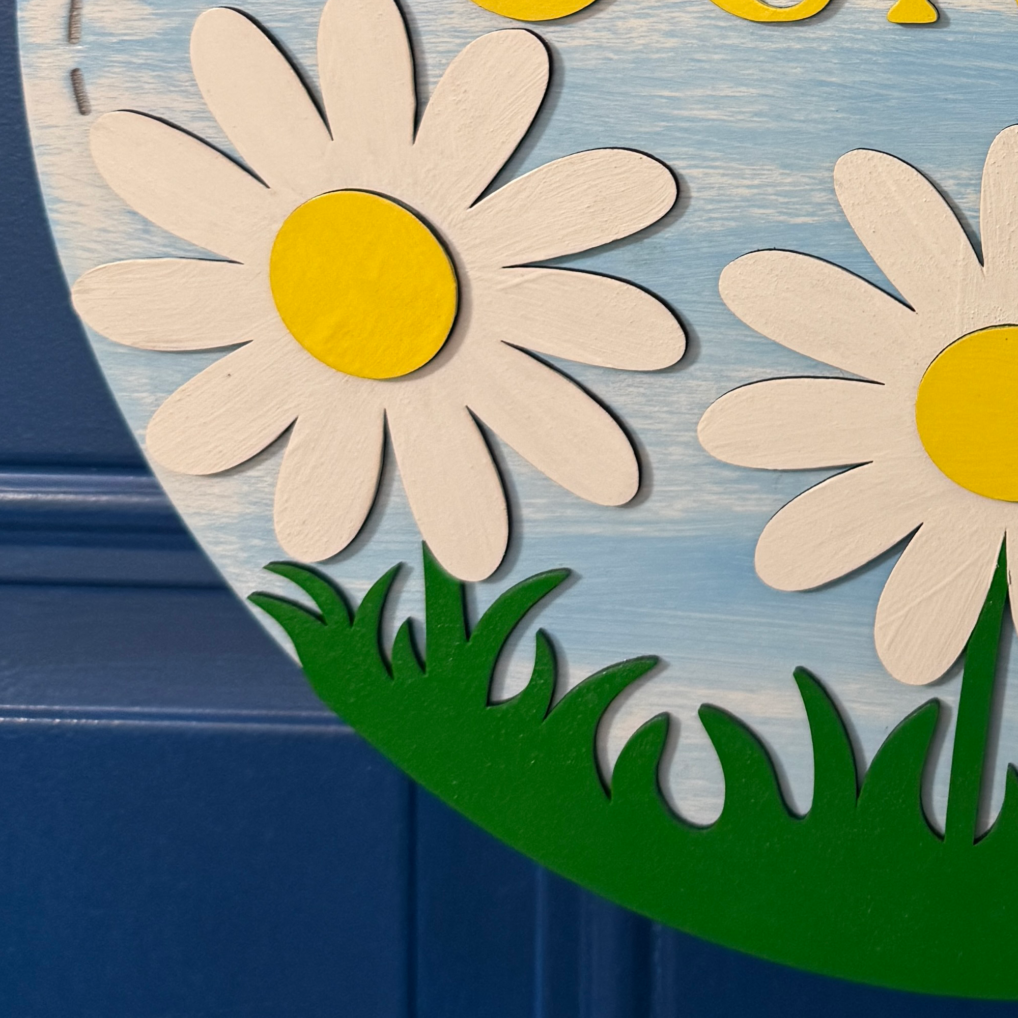 Close-up of white daisy flowers with yellow centers and green grass detail on wooden door hanger