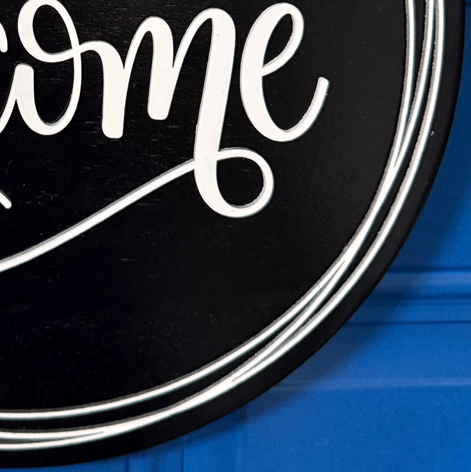 Close-up of white welcome script lettering on black painted wood door hanger with layered border detail