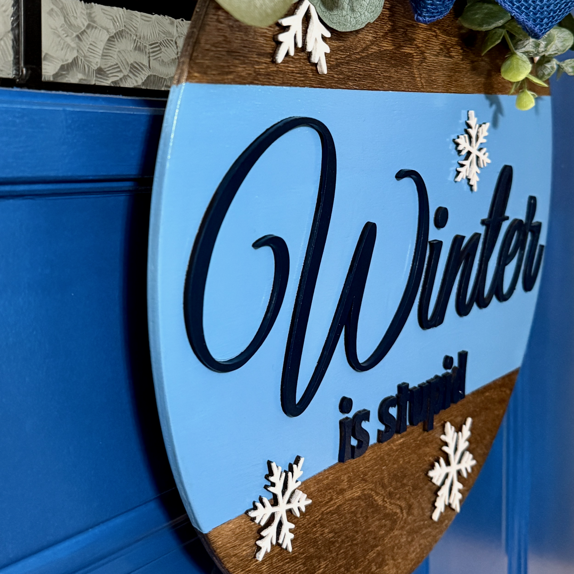 Close up of layered white snowflake accent on the lower portion of Winter Is Stupid wooden door hanger
