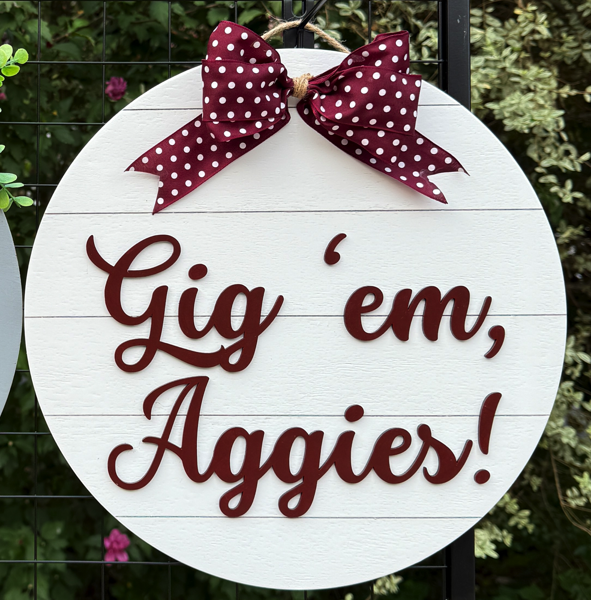Round Gig ’em Aggies door hanger with maroon script on white shiplap background and maroon polka-dot bow