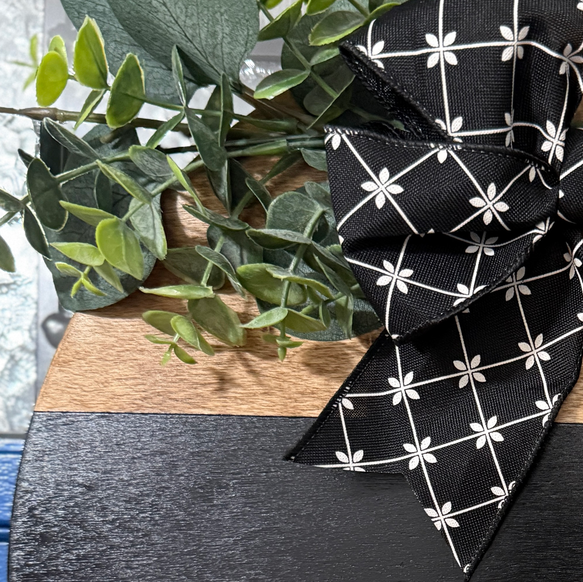 Close-up of greenery and black patterned ribbon bow attached to handcrafted oh hey wood door hanger