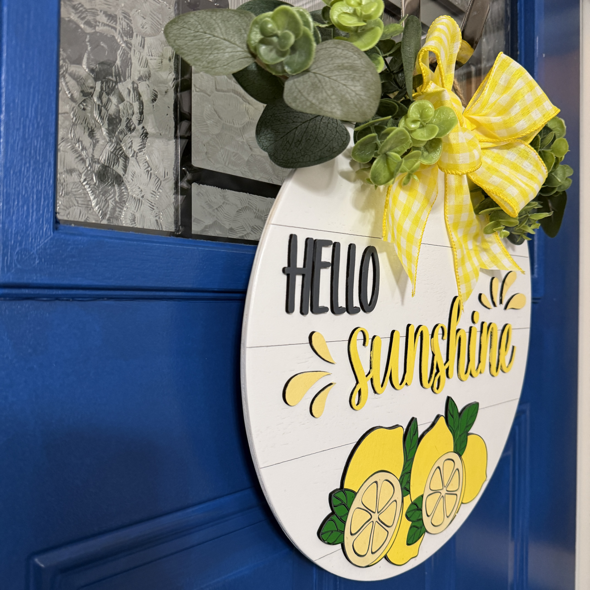 Angled side view of Hello Sunshine round wood door hanger showing layered thickness, greenery, and dimensional lettering