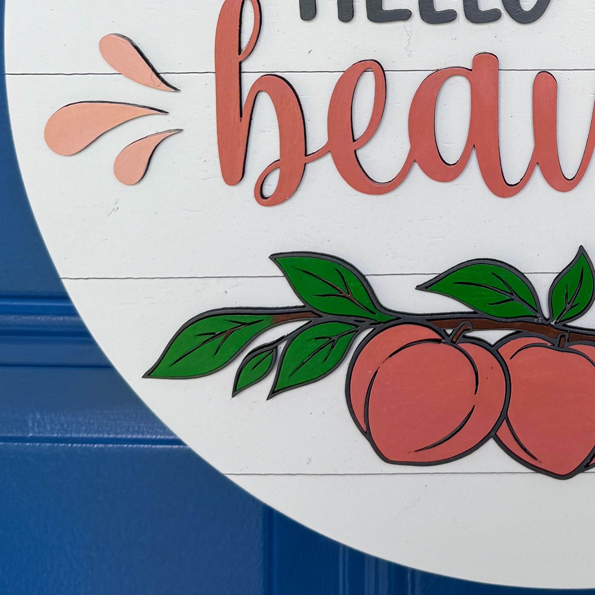 Close-up of layered wood peaches, greenery, and Hello Beautiful lettering on a handmade farmhouse-style door hanger.