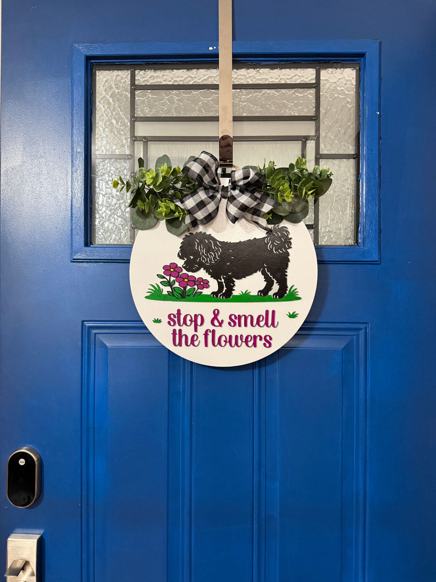 Full view of Stop and Smell the Flowers spring dog door hanger displayed on bright blue front door with buffalo check bow