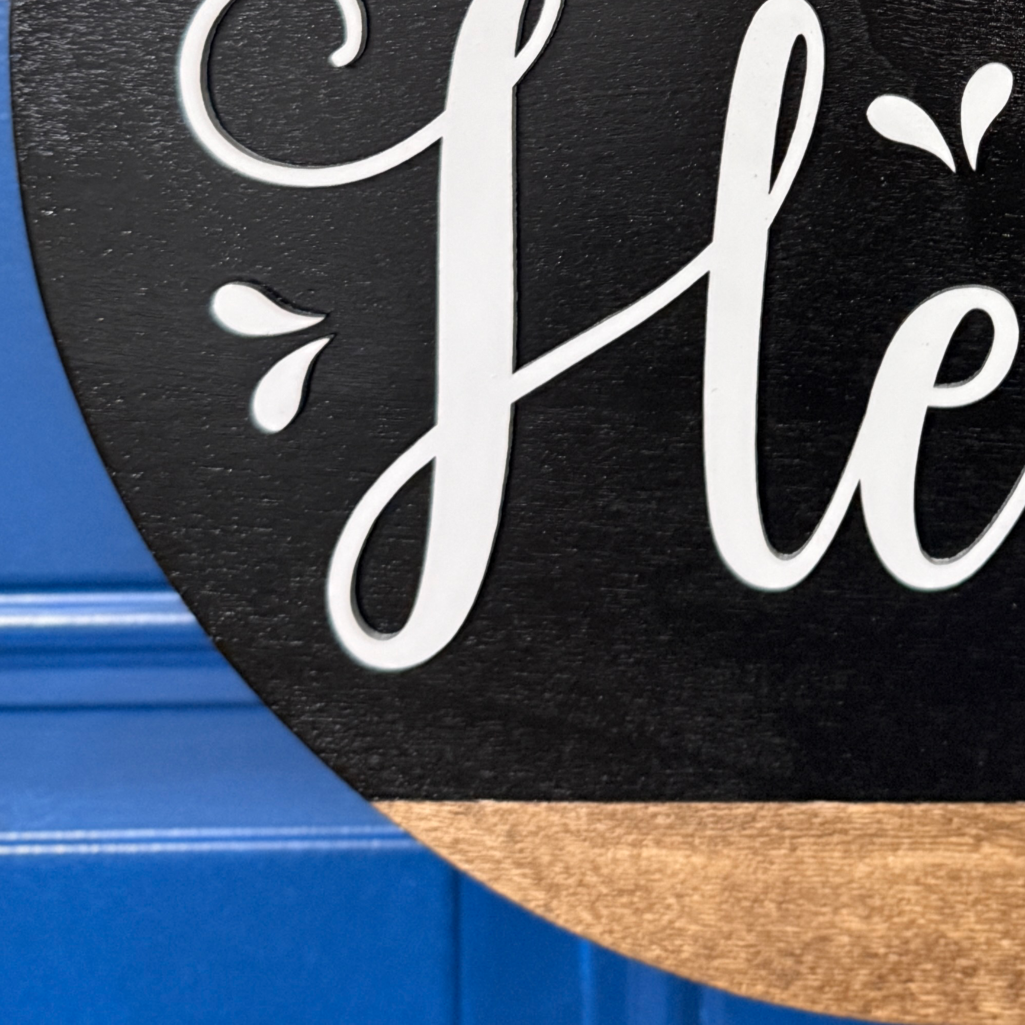 Close-up of white Hello script lettering on black painted wood door hanger with natural wood accent