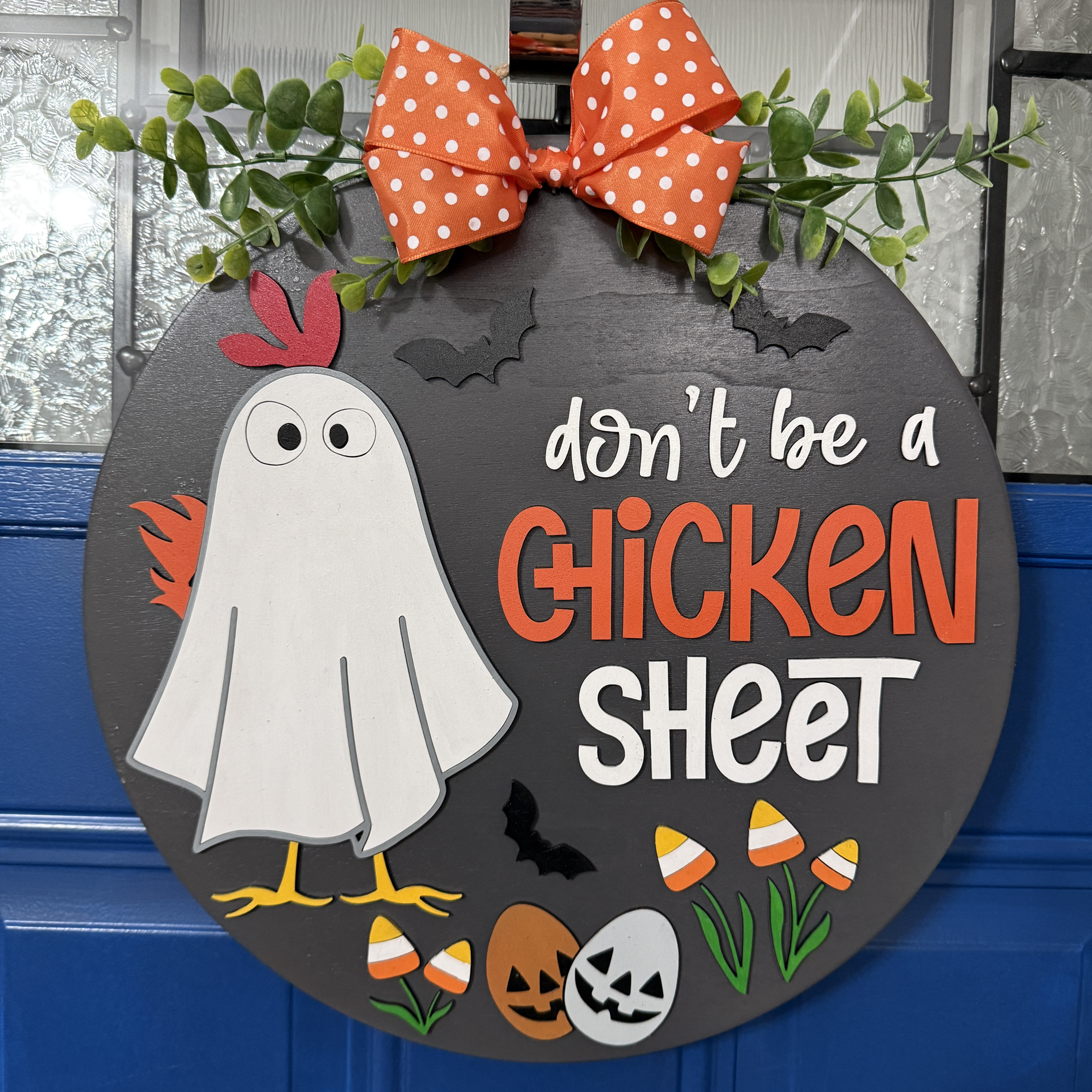 Front view of Halloween door hanger with ghost chicken, candy corn accents, and phrase “Don’t Be a Chicken Sheet” in bold letters