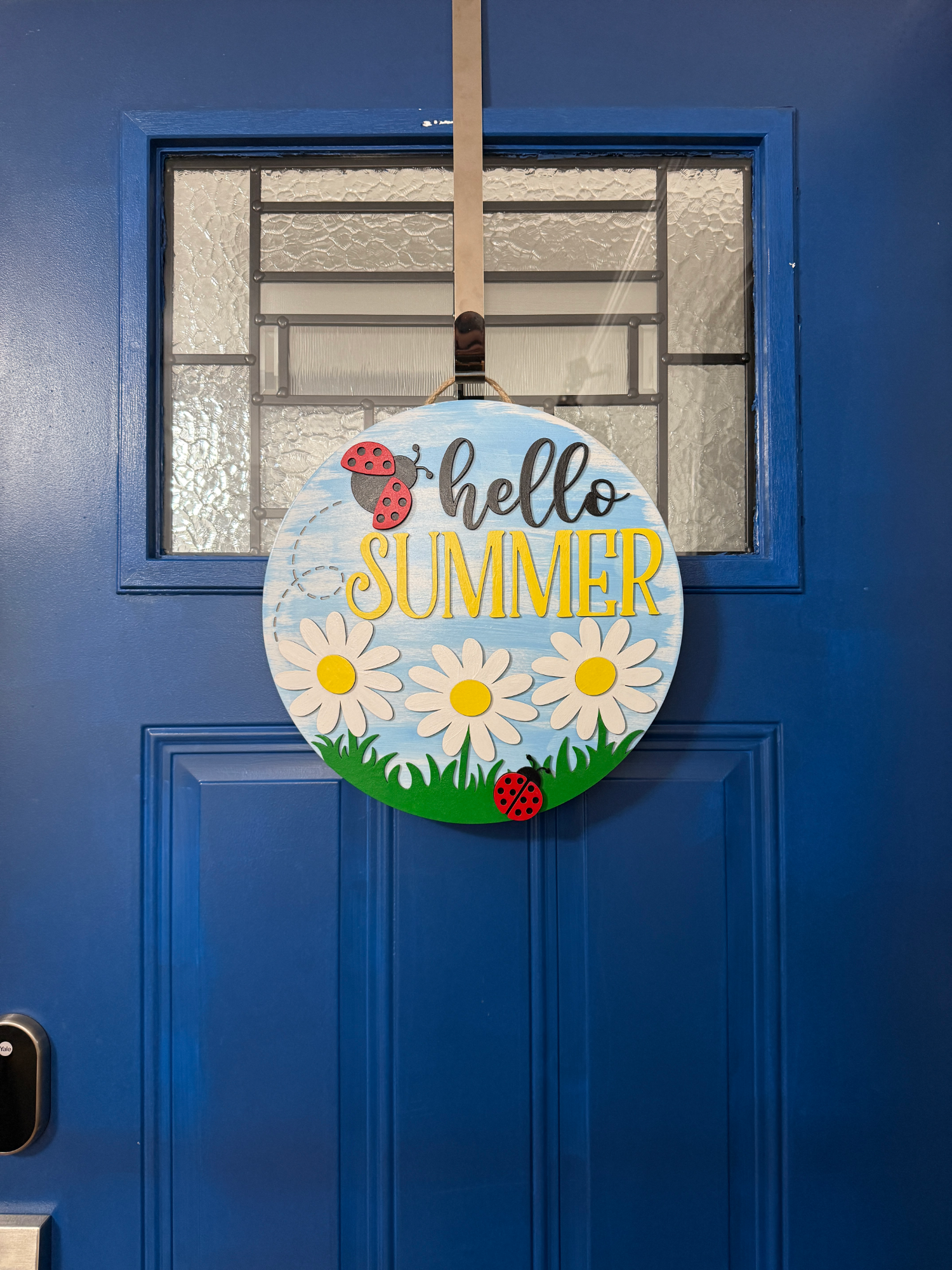 Full door view of hello summer sign hanging on blue front door with glass panel