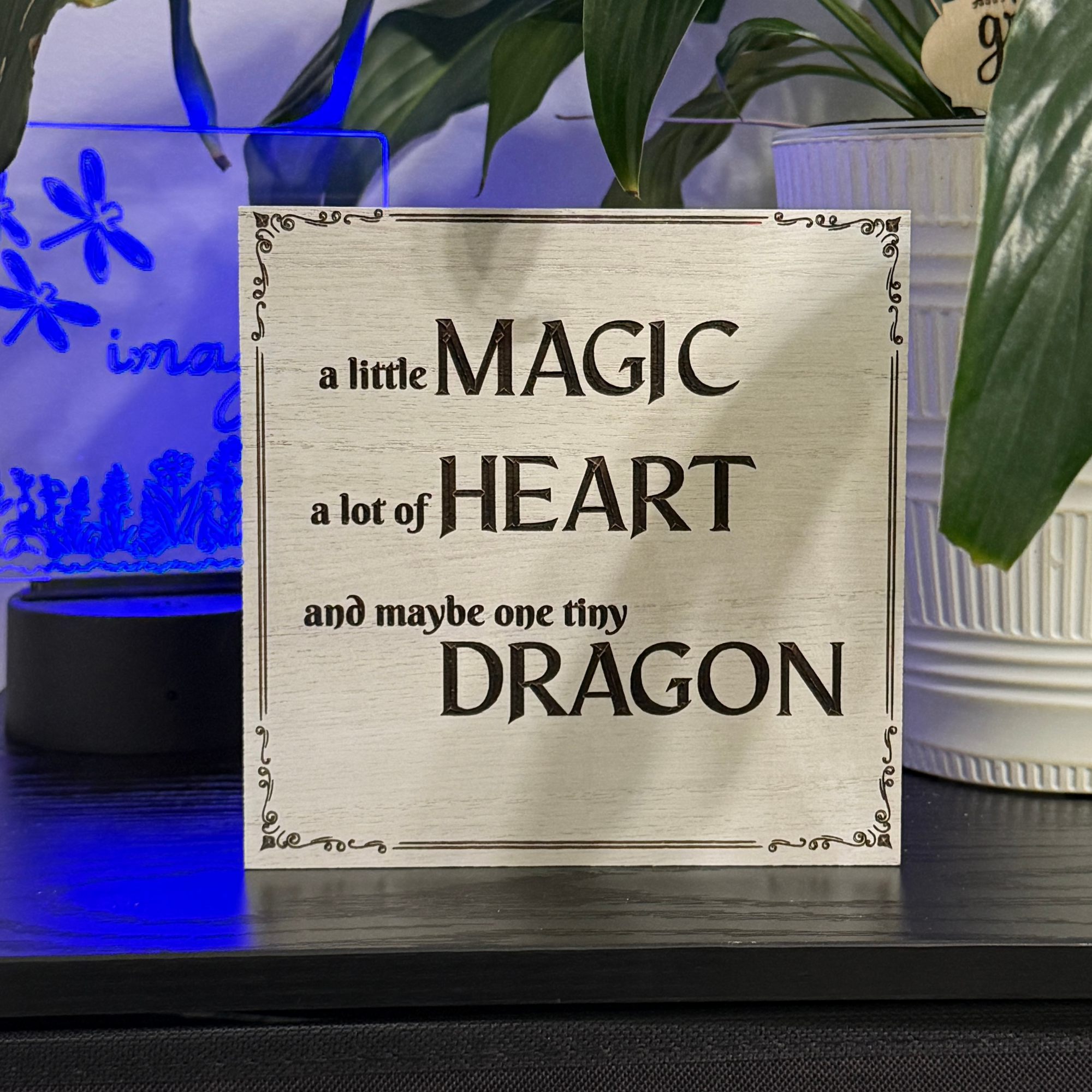 Wooden sign reading a little magic a lot of heart and maybe one tiny dragon displayed with blue accent lighting