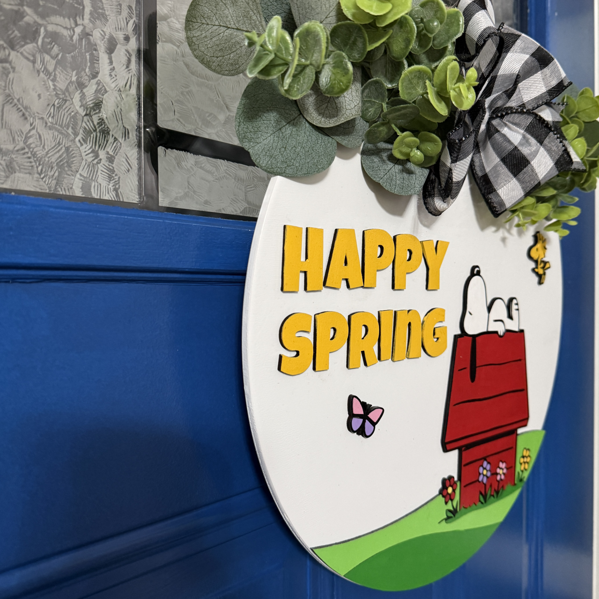 Angled side view of spring door hanger showing layered wood design and greenery bow accent