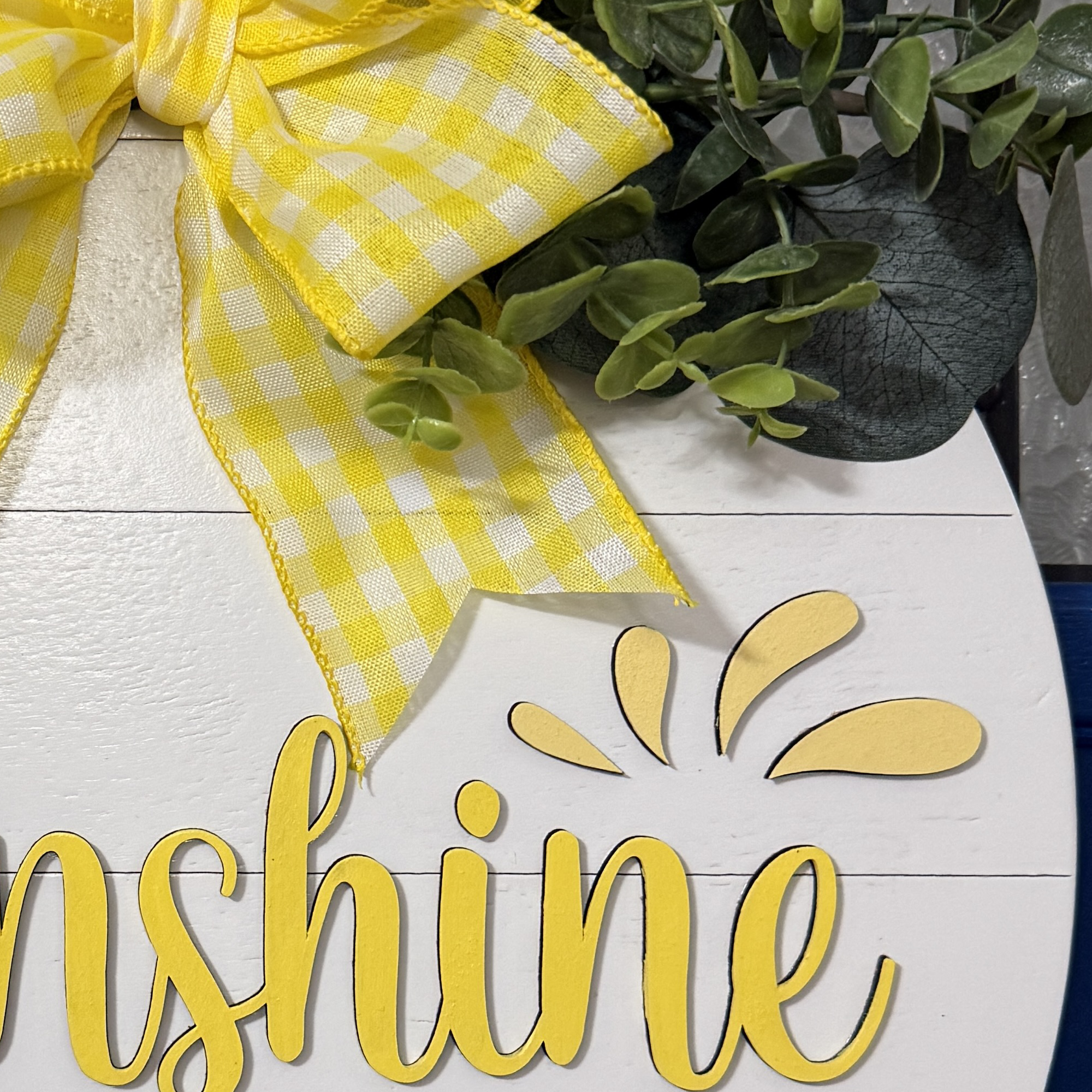 Detailed view of yellow gingham bow and layered greenery on top of lemon-themed summer door decor