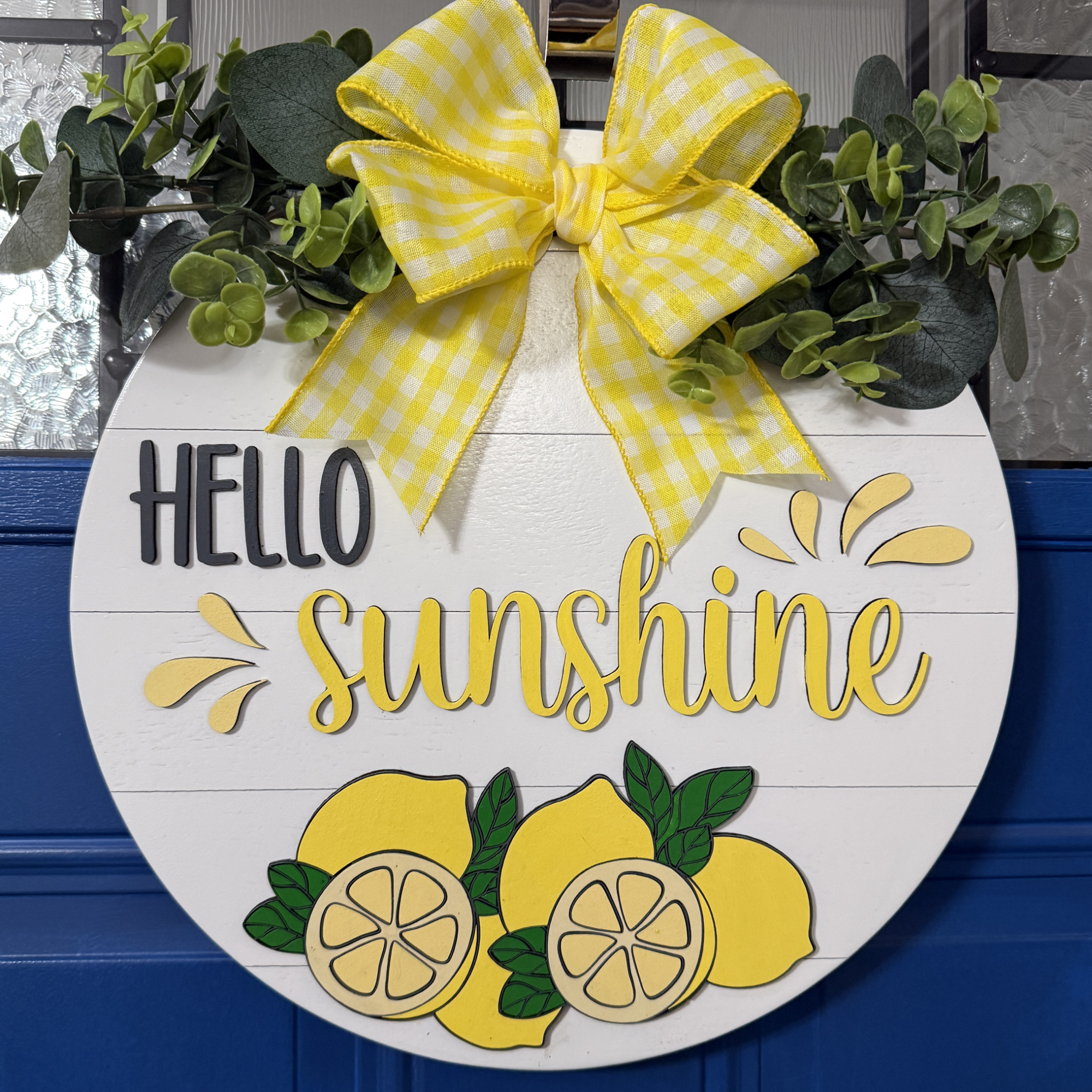 Front view of Hello Sunshine lemon door hanger with raised yellow lettering, hand-painted lemons, and yellow gingham bow on blue door