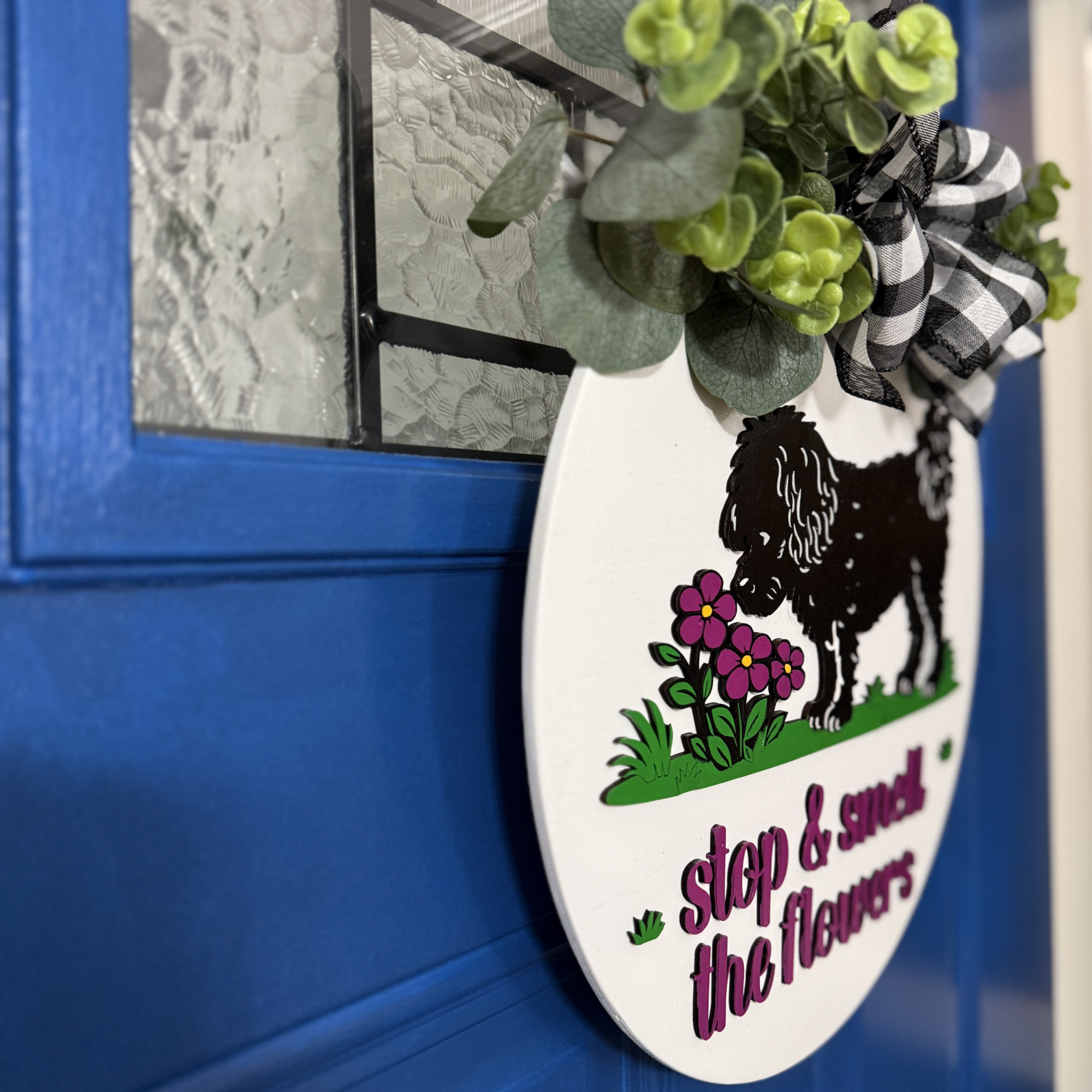 Angled side view of round wood dog door hanger showing layered thickness, greenery detail, and raised lettering