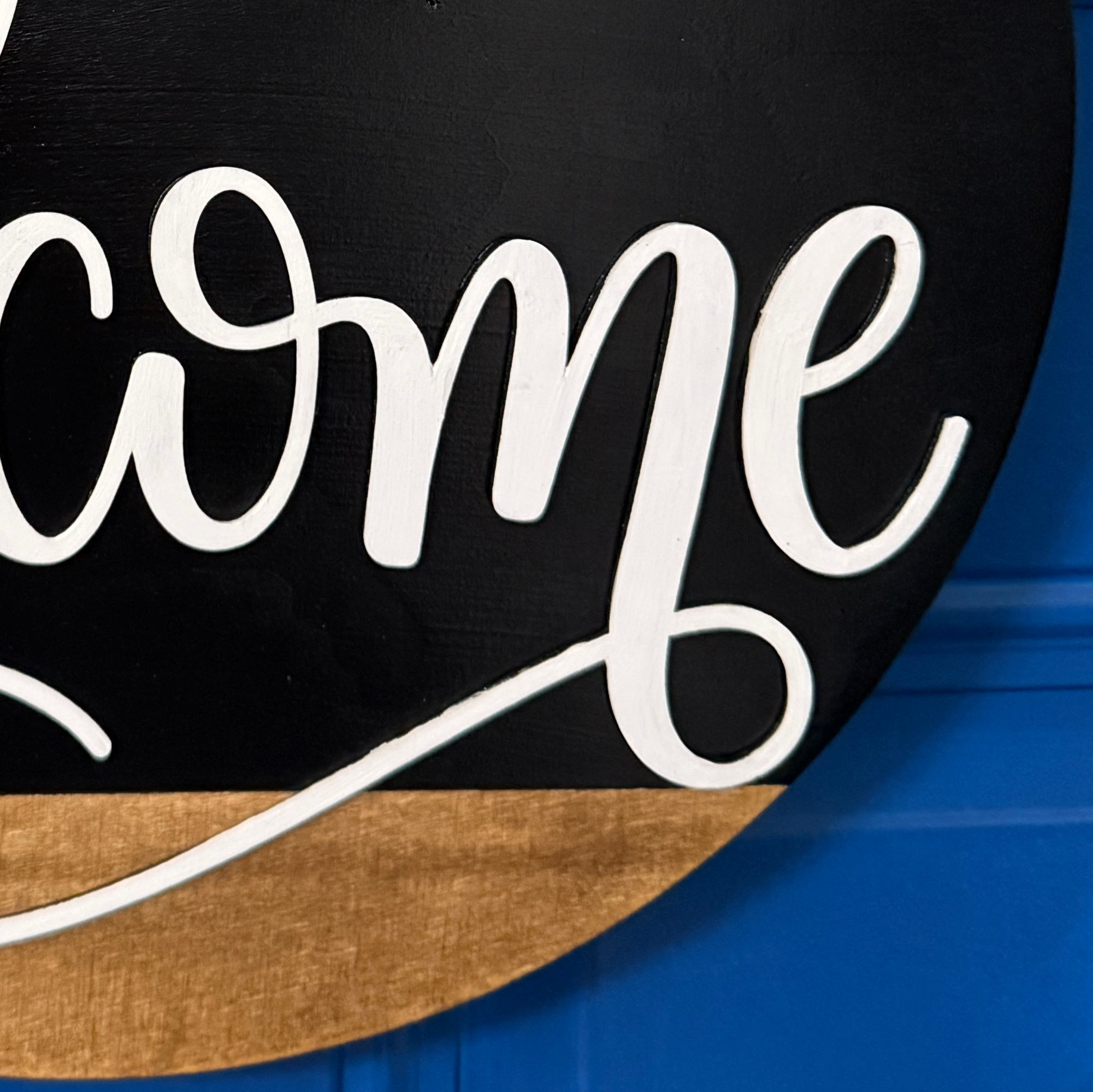 Close up of Welcome door hanger on stained base with black background, faux with greenery and coordinating bow