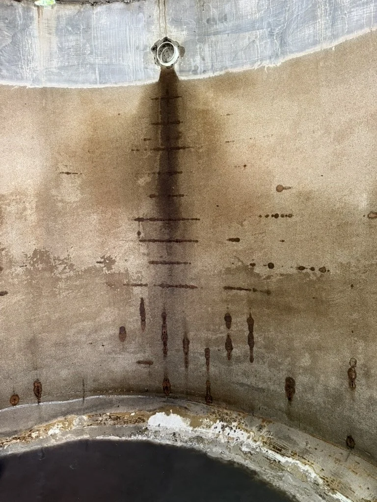 Internal surface of a concrete tank clearly showing rust spots following internal reinforcing along with a clear high water line where the plaster lining above the water is still in good condition.