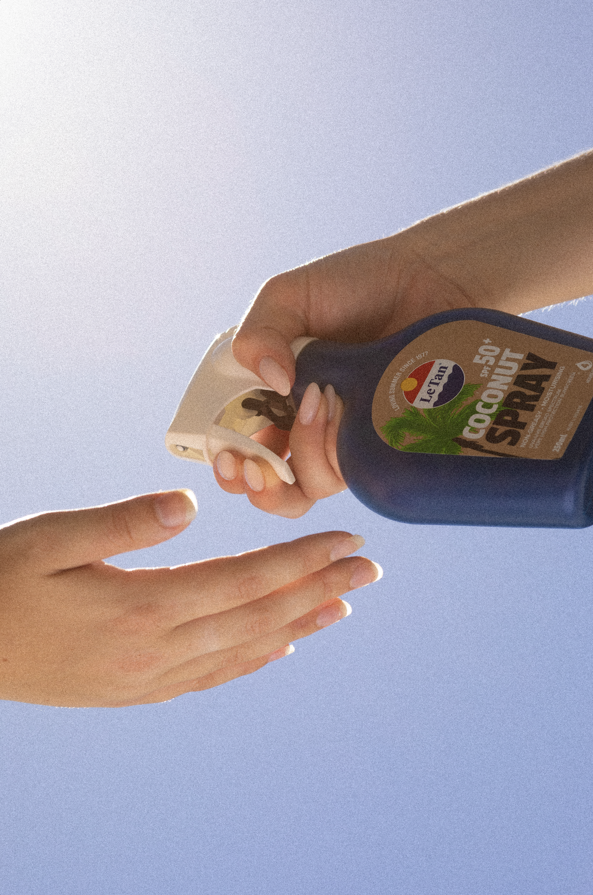 Person spraying sunscreen on hands against a blue sky background.