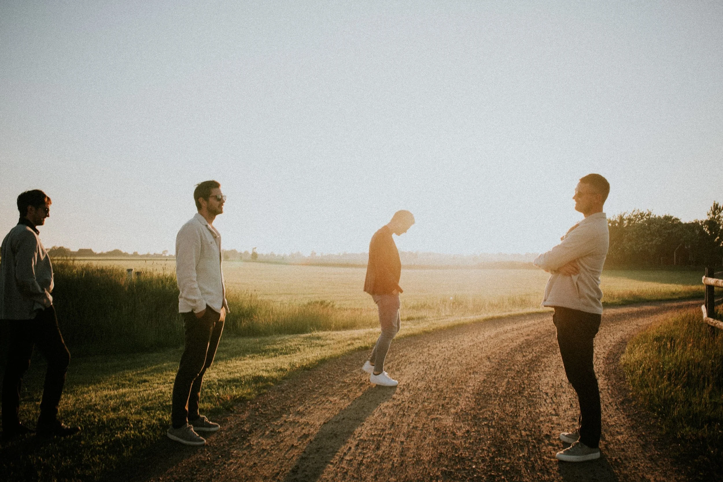 Four men standing on a dirt path in a rural setting during sunset, with grassy fields in the background. LiveFlotten Malmö. Malmö City. Summer in Malmö. Flotten Malmö. Malmösommar. Vår i Malmö Spring Malmö