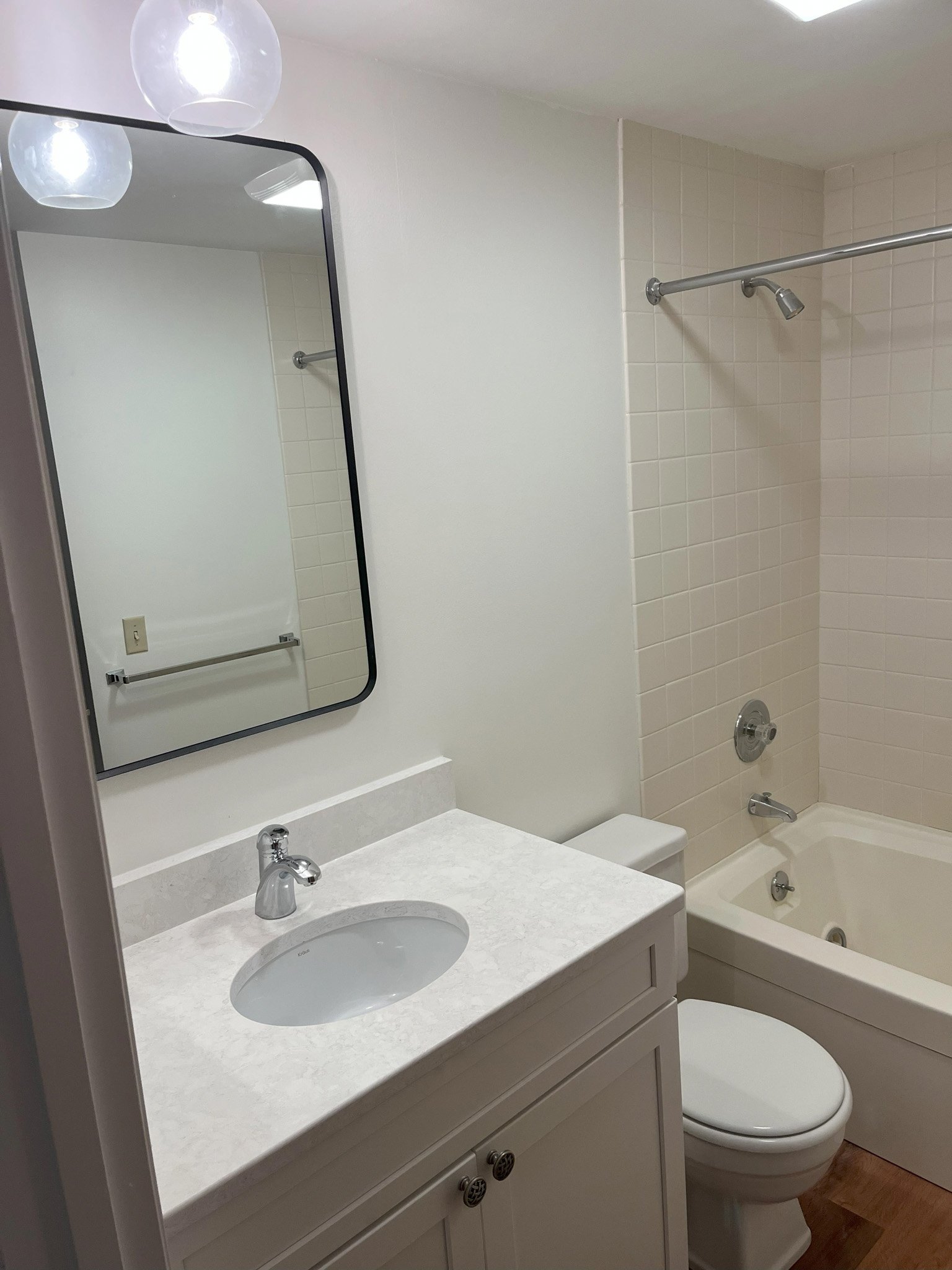 A bathroom with a white vanity, oval sink, mirror, toilet, bathtub with shower, and light fixtures.