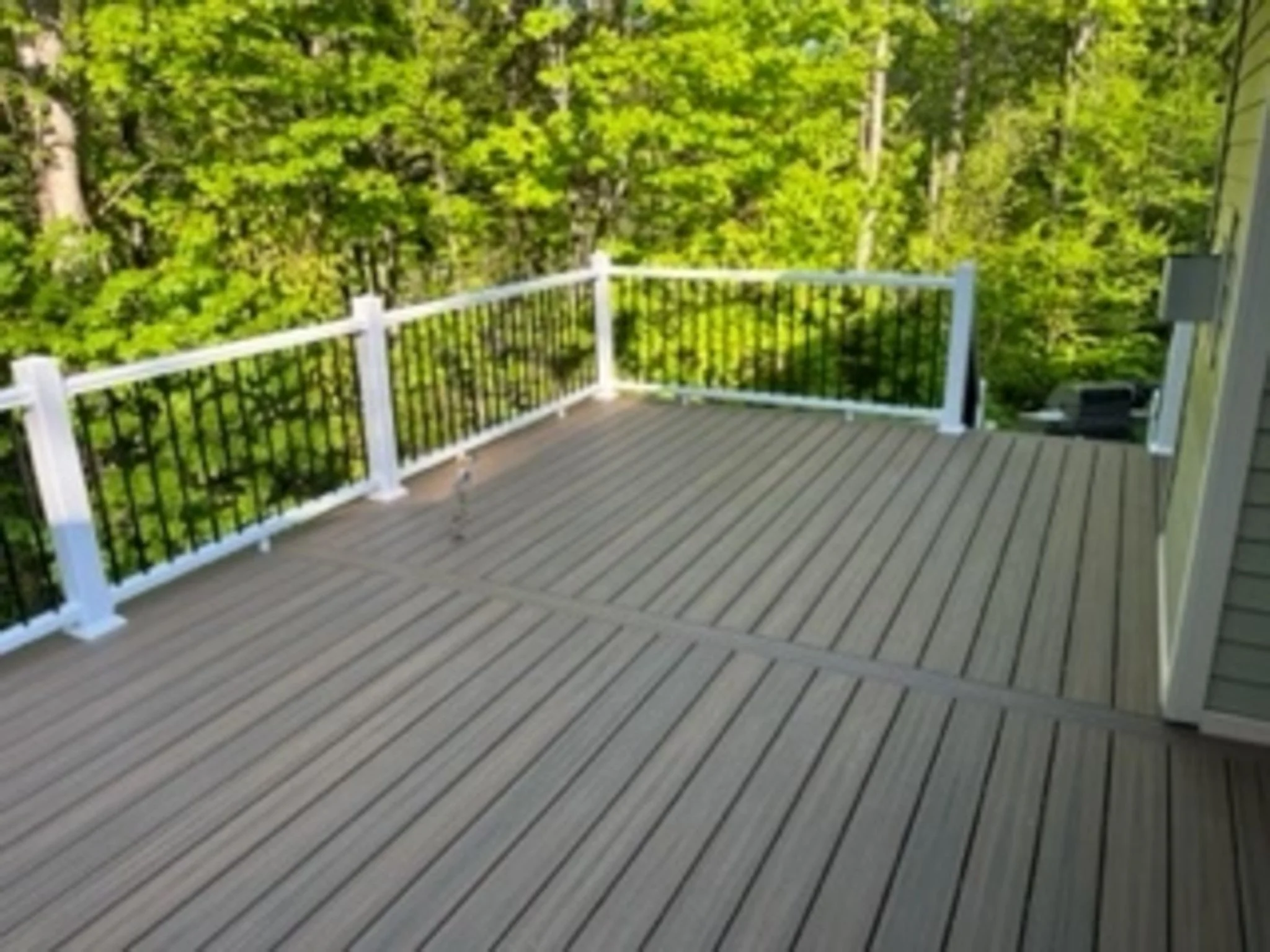 Wooden deck with white and black railing, surrounded by green trees.