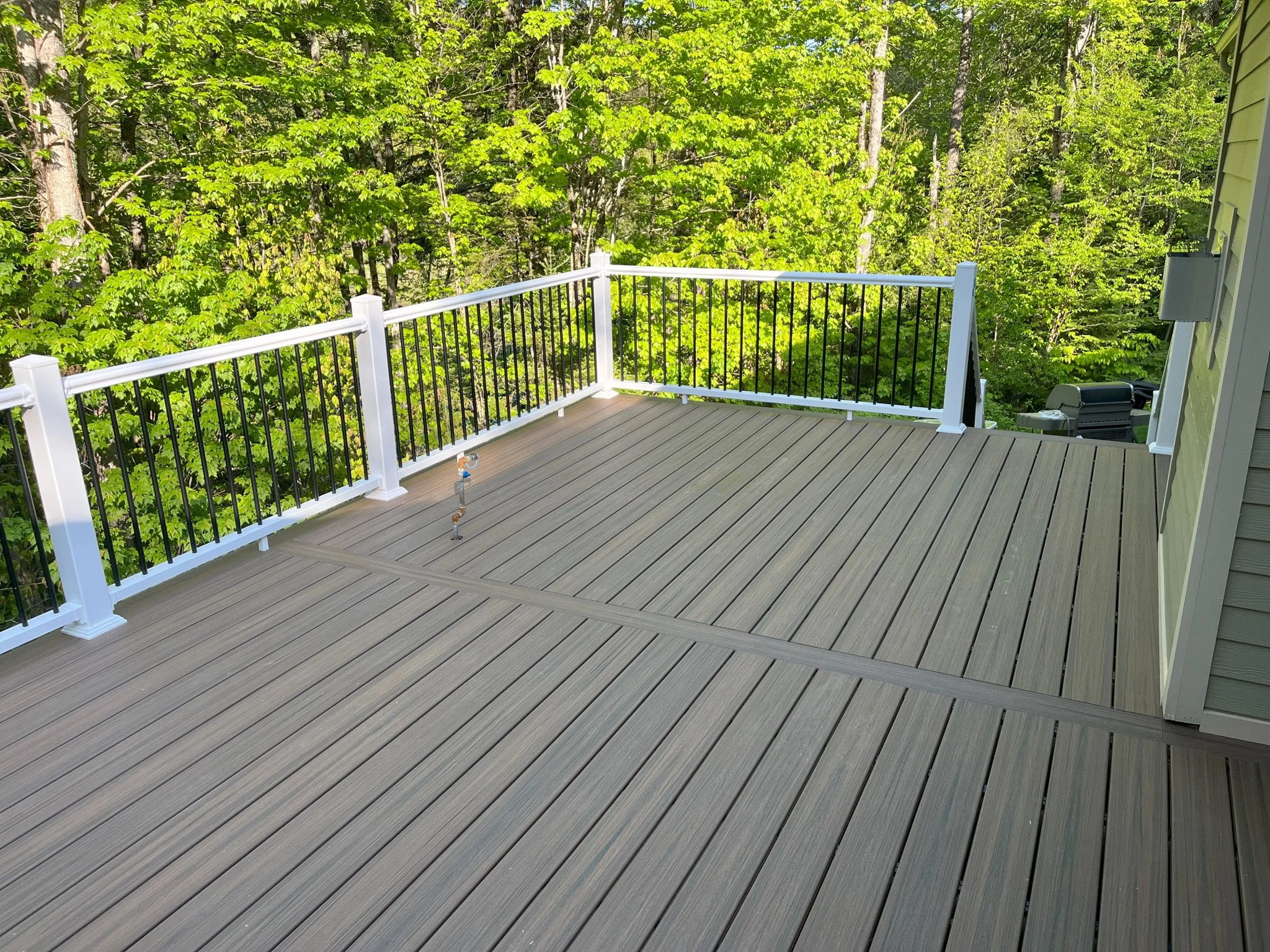 Empty wooden deck with a black and white railing overlooking a lush green forest.