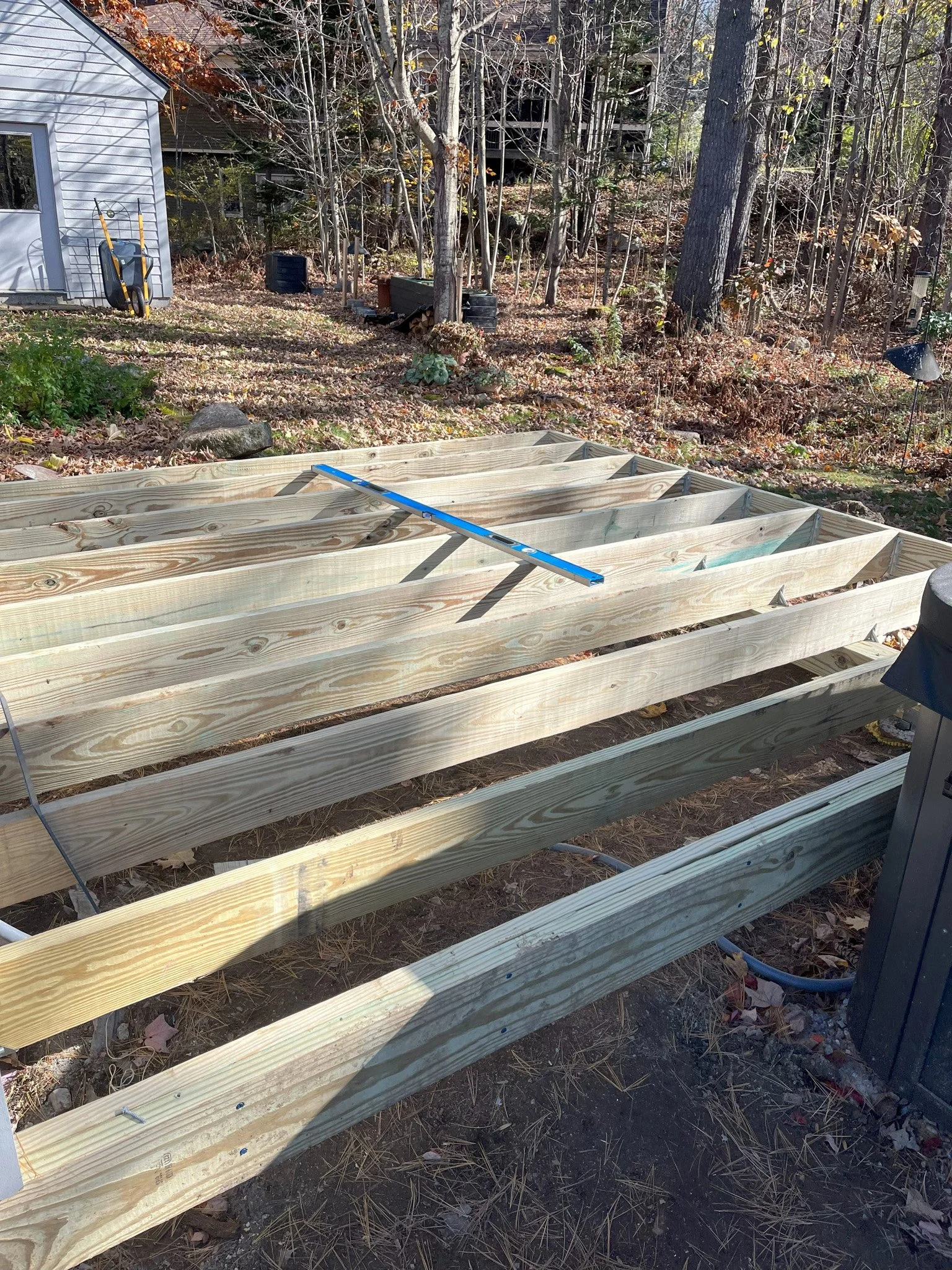 Wooden deck framing under construction in a backyard with trees and a shed.