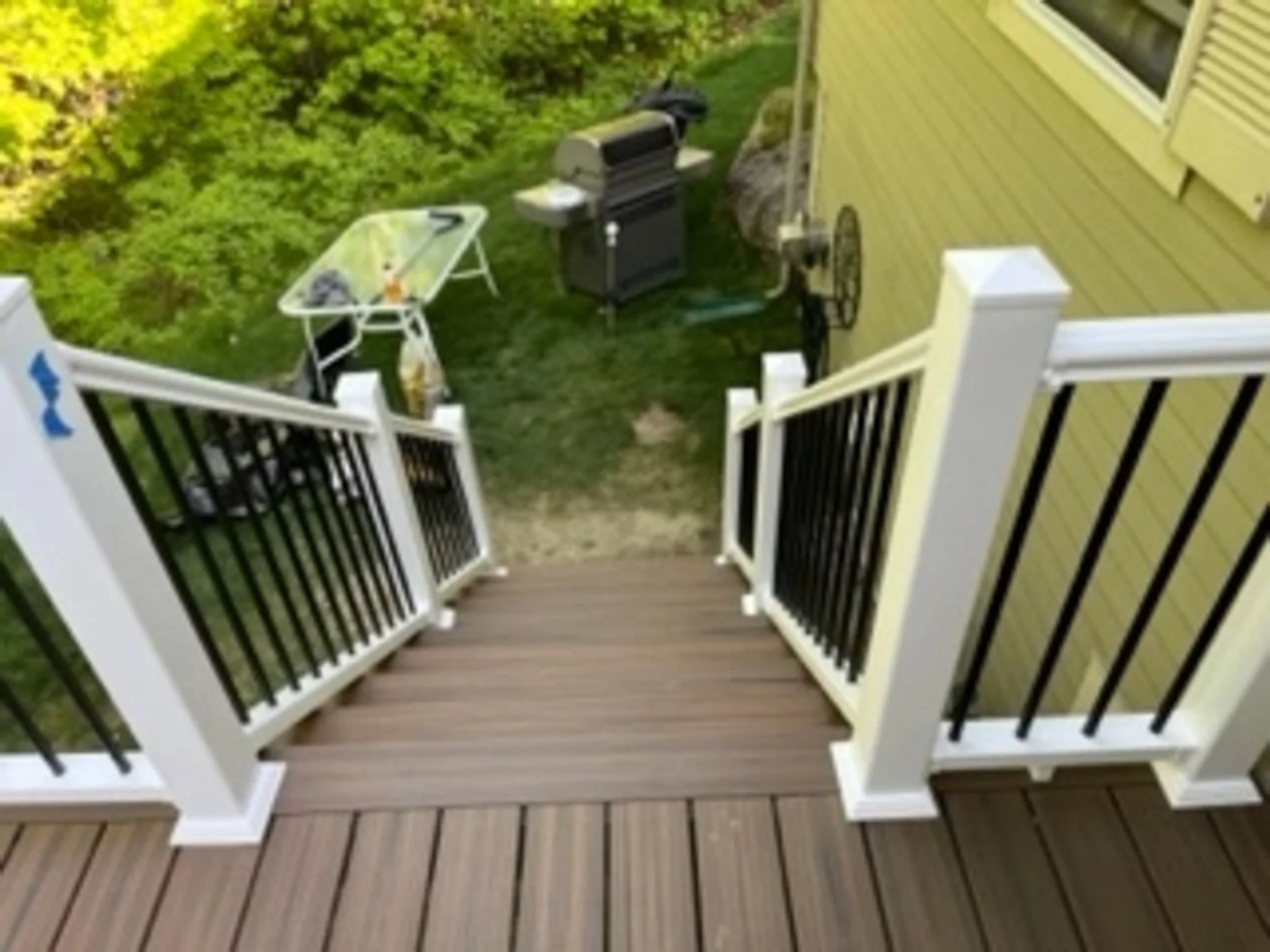 View from a deck overlooking a backyard with a grill, a table with items, and green foliage.