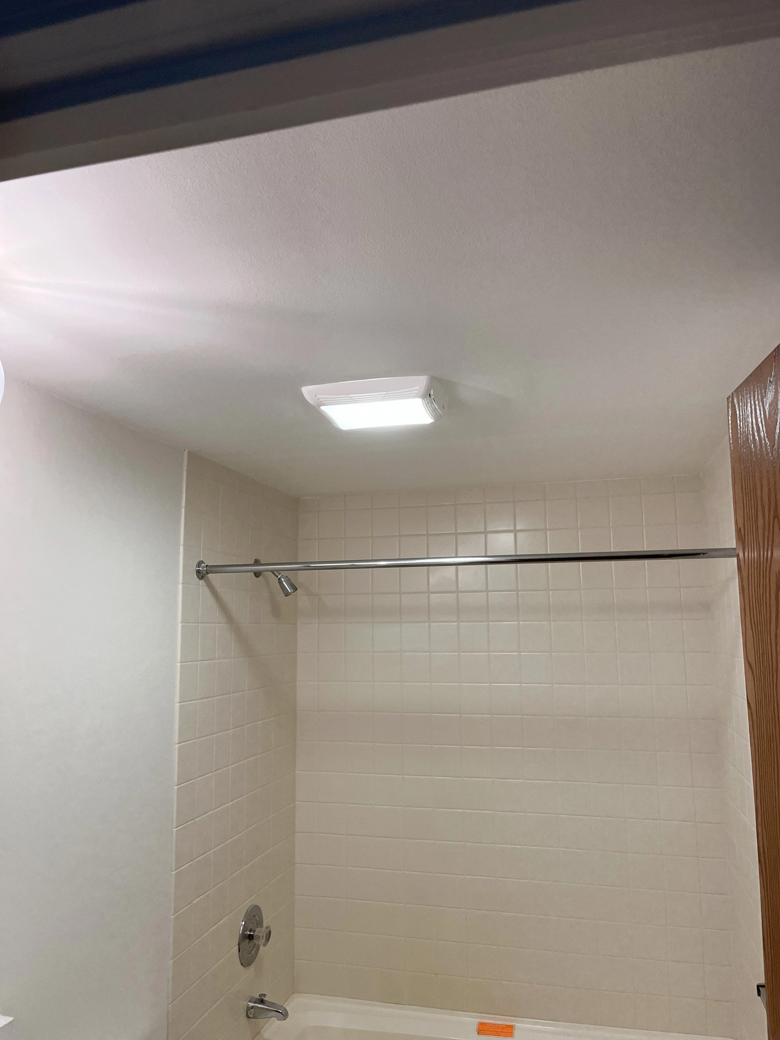Empty shower with a metal shower rod, a showerhead, and a bathtub with a soap dish, tiled walls, a ceiling light, and a ceiling vent.