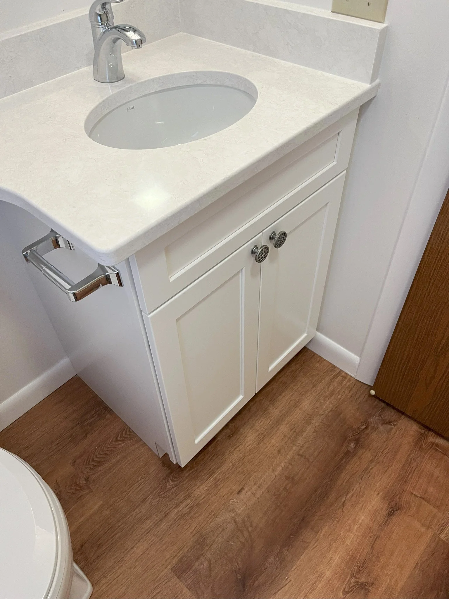 A white bathroom vanity with a marble countertop, an oval sink, a chrome faucet, a towel bar on the side, and wooden flooring.