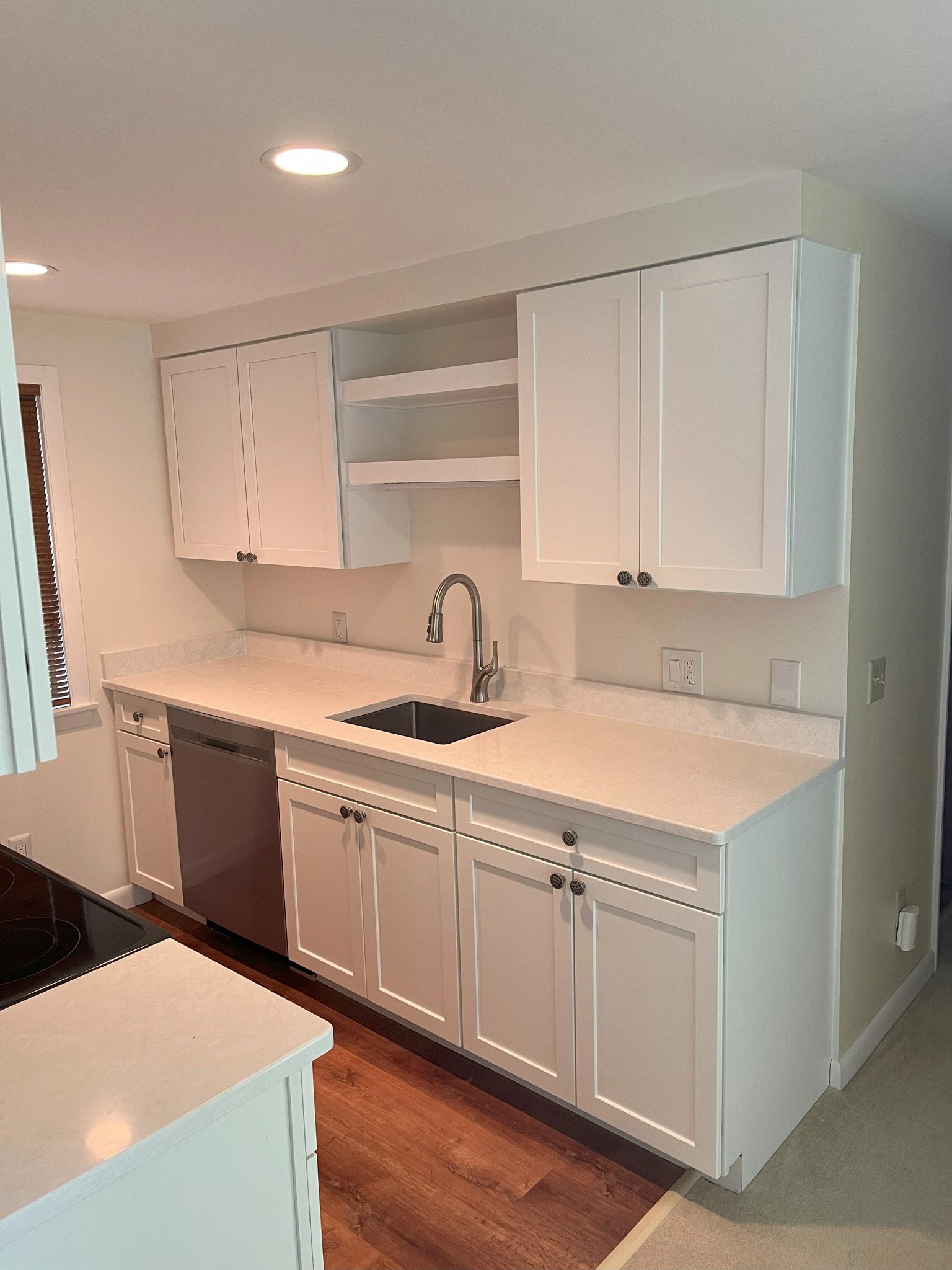 A modern kitchen with white cabinets, a black sink, stainless steel dishwasher, and open shelves above the counter.