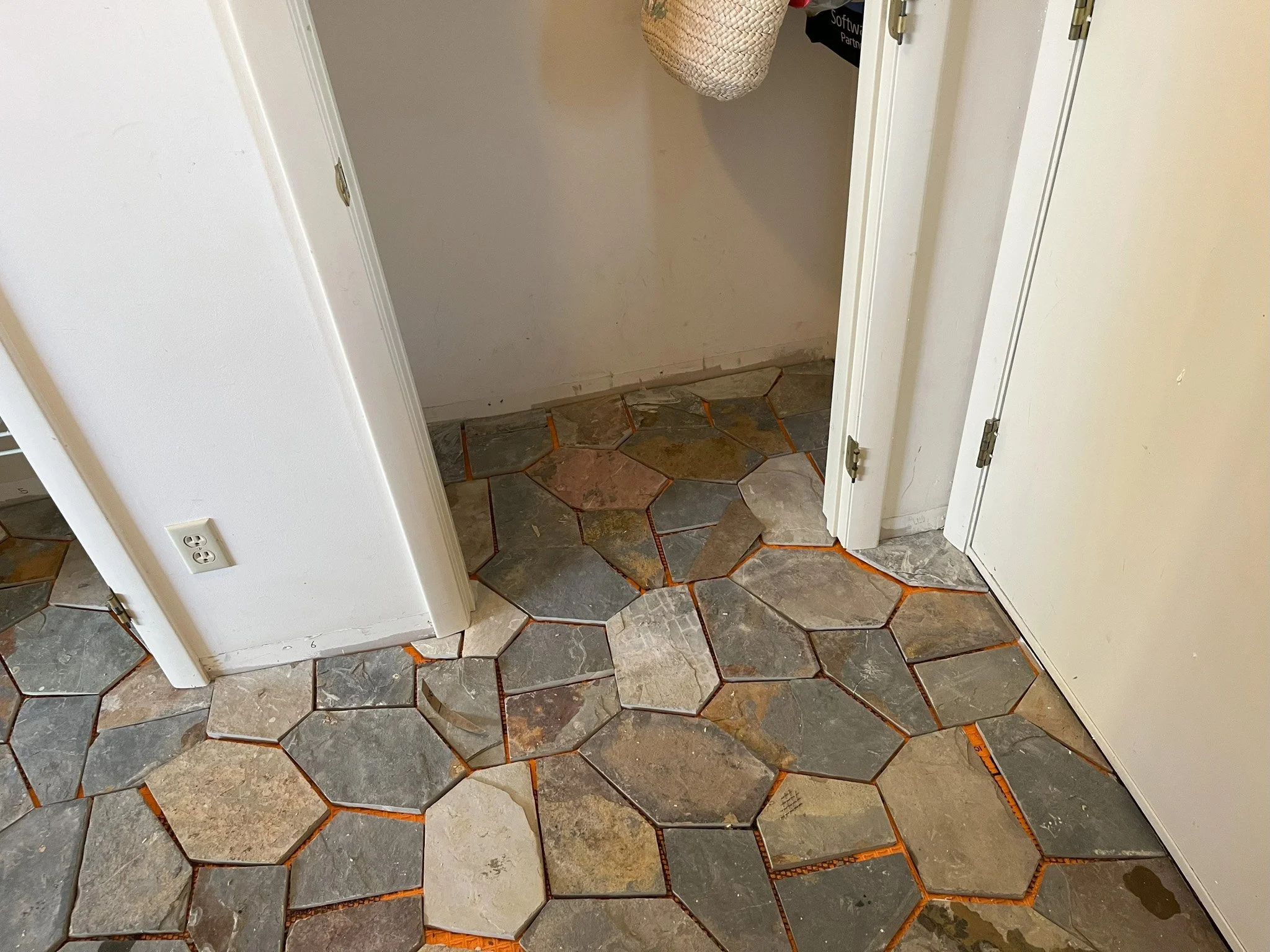 Bathroom or laundry room with slate tile flooring in various shapes and sizes, with orange grout and a small patch of water on the floor.