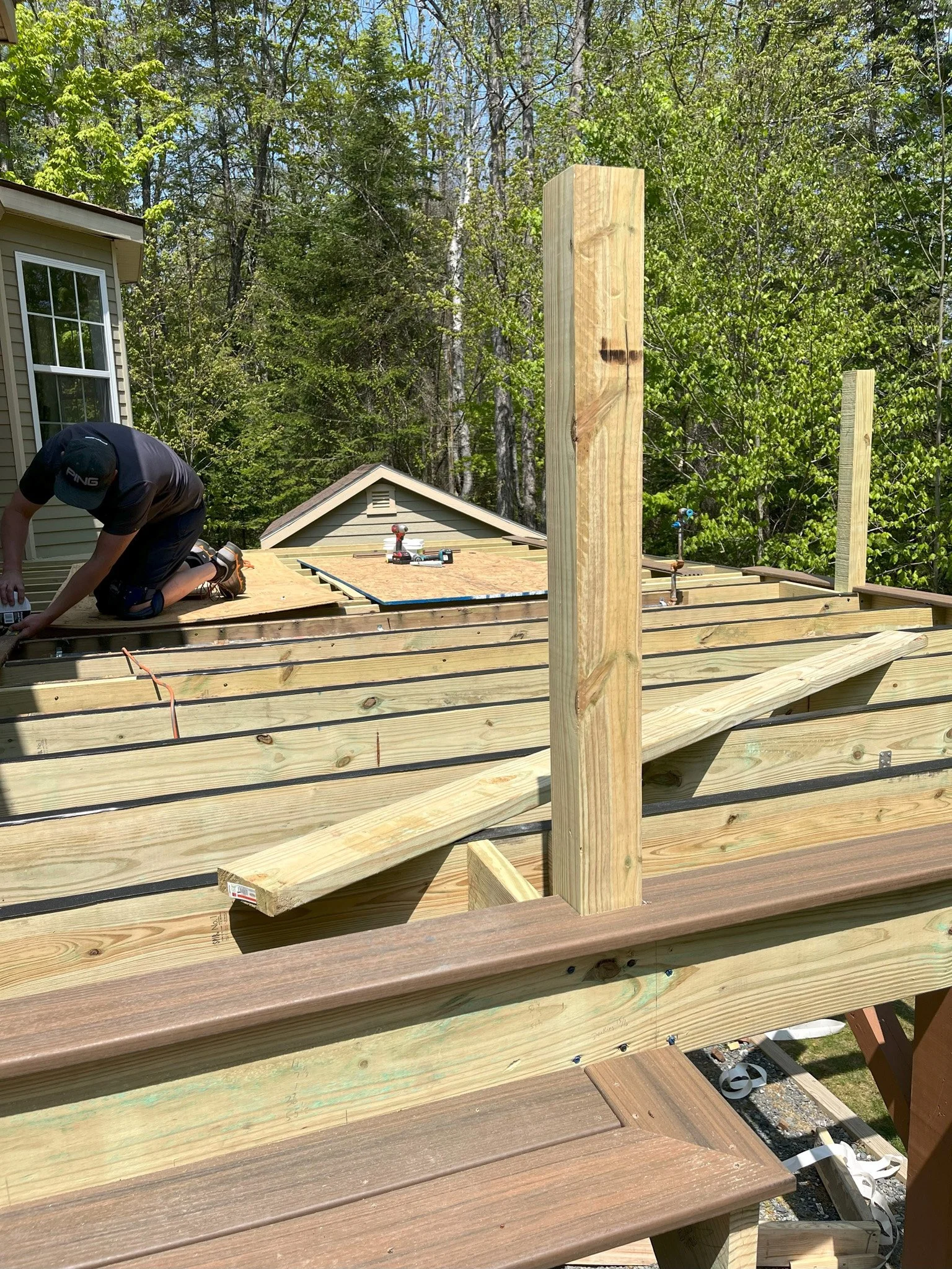 Construction worker installing decking on a wooden deck in a backyard, with trees in the background.